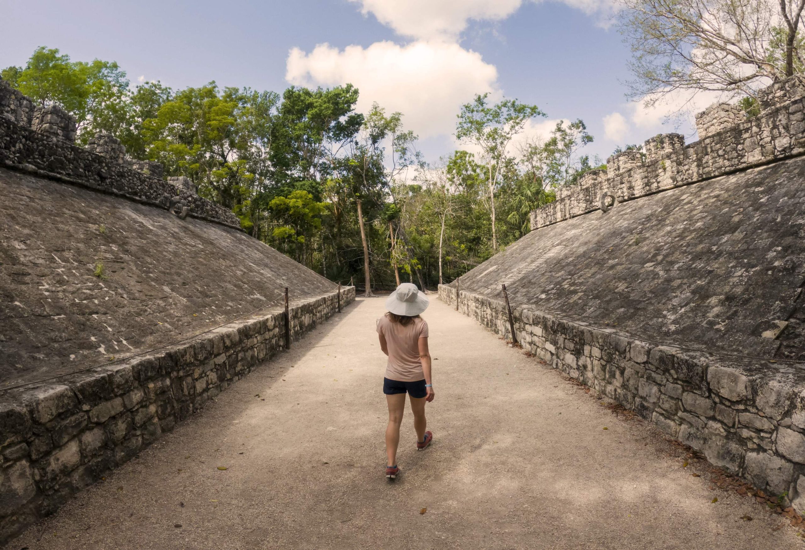 Person walking between two structures at Coba mayan ruins with tropical jungle in background