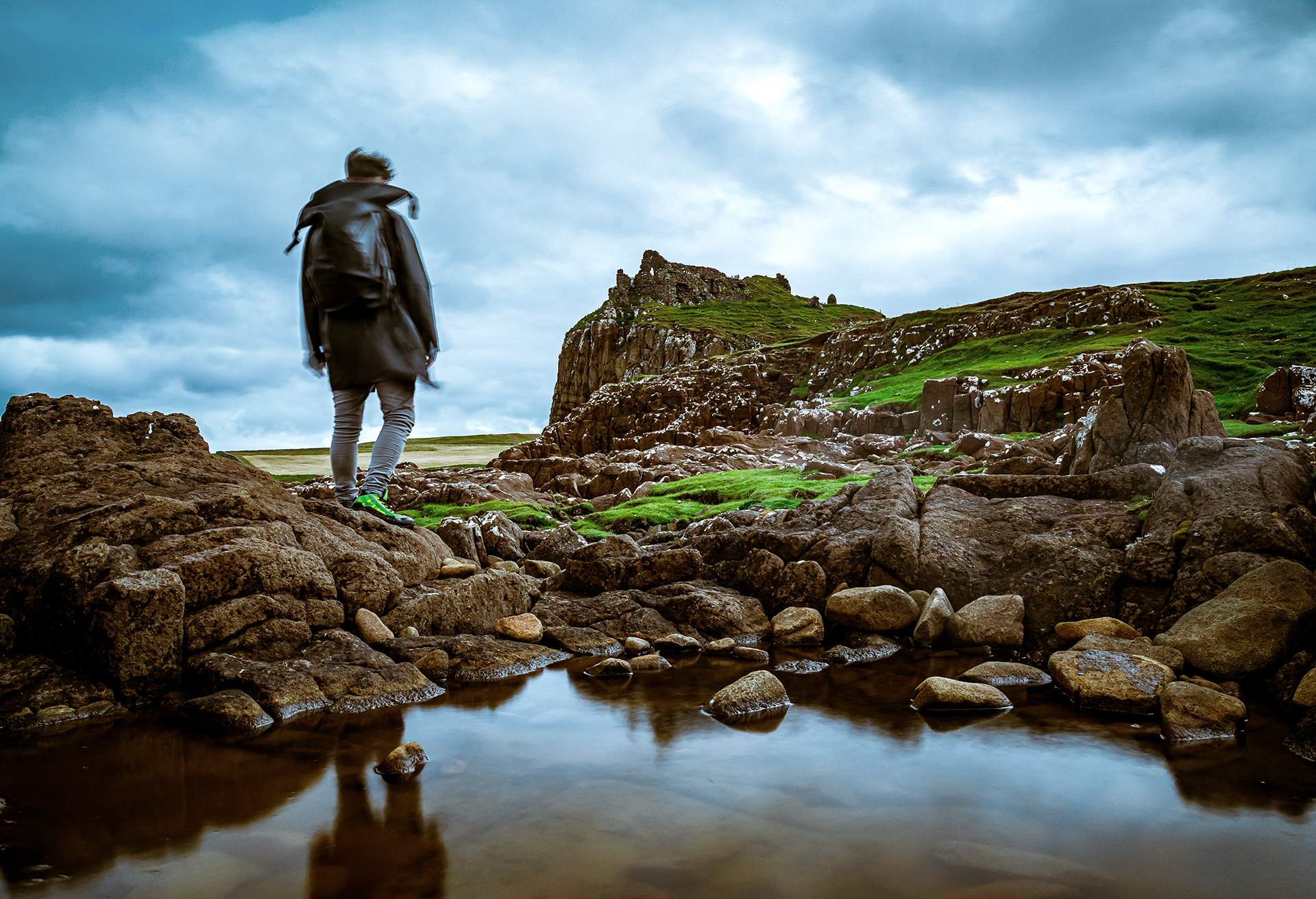 MAN LOOKING AT RUINS OF DUNTULM CASTLE ON THE ISLE OF SKYE, SCOTLAND