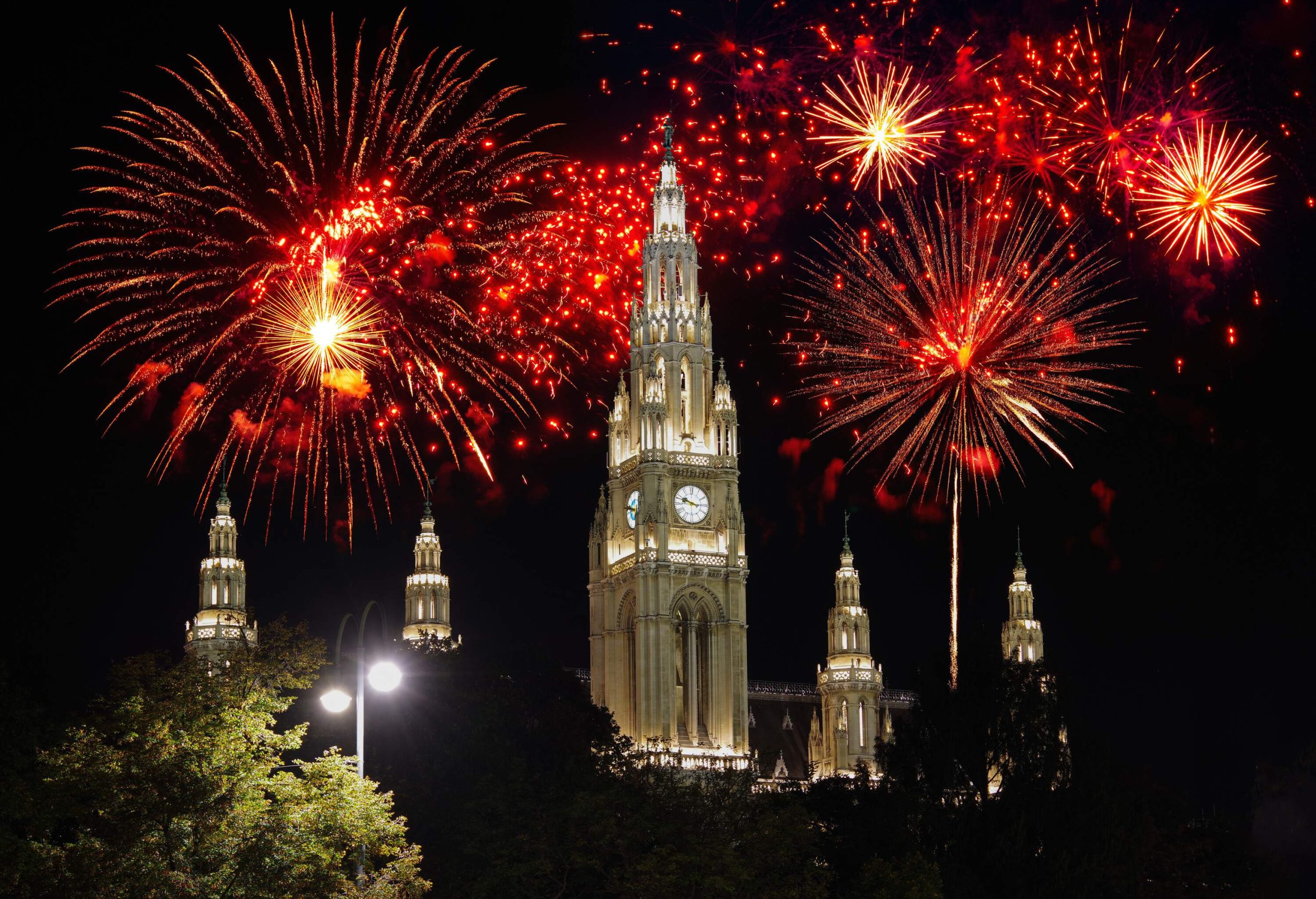 Red colored fireworks rising above some church towers