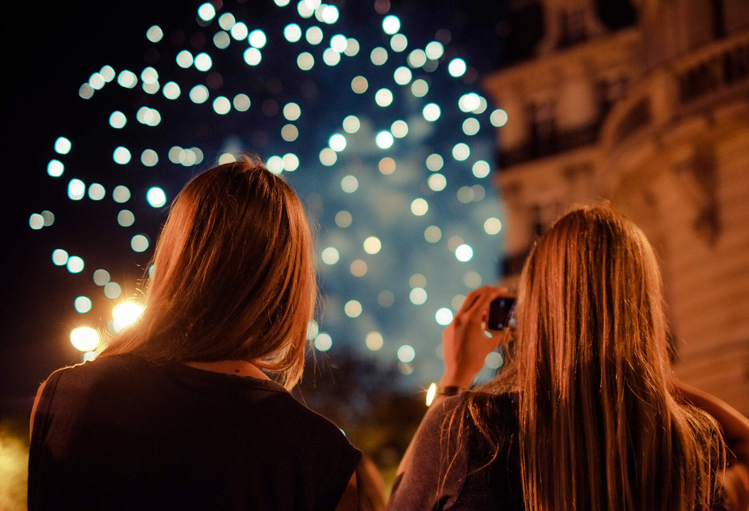 A person stares up at the sky full of fireworks while another snaps a photo.