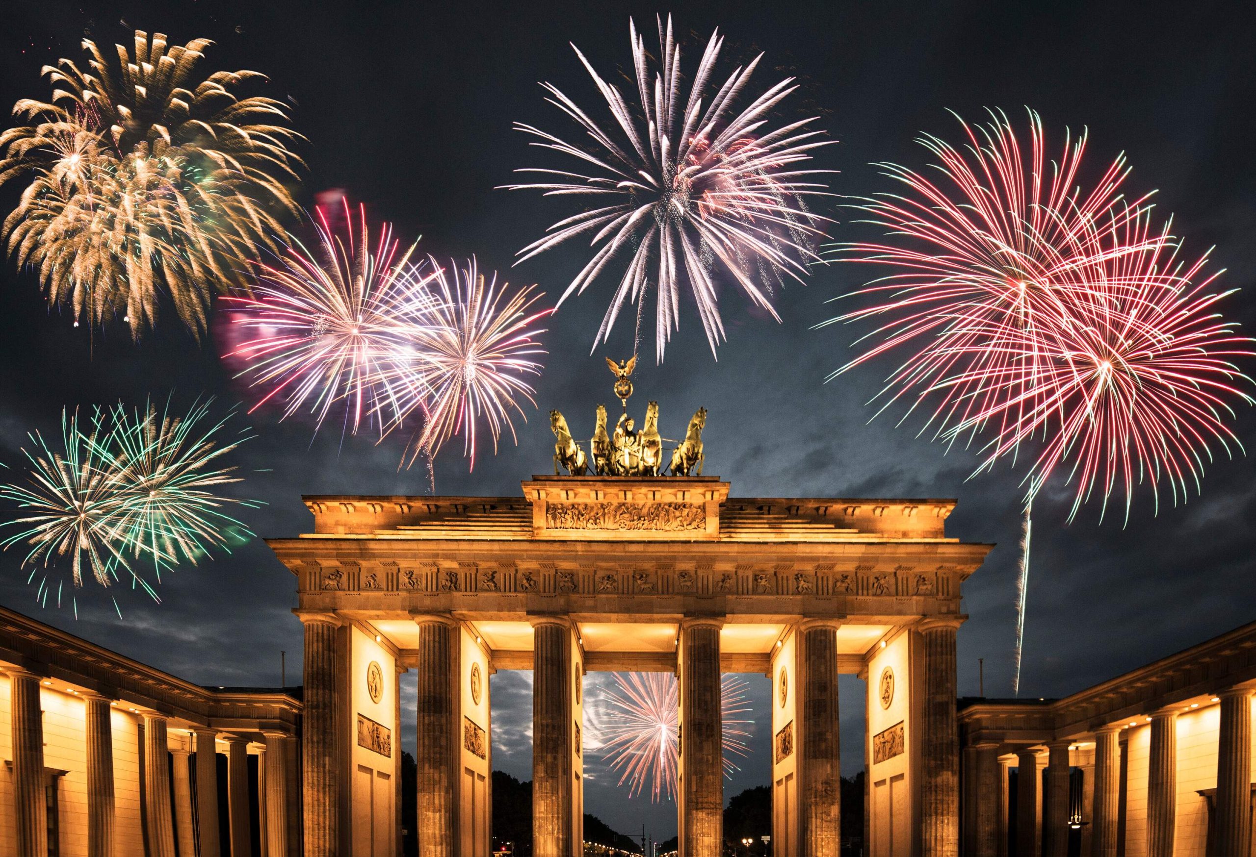 Colourful fireworks explode in the night sky as seen from the illuminated Brandenburg Gate in Berlin.