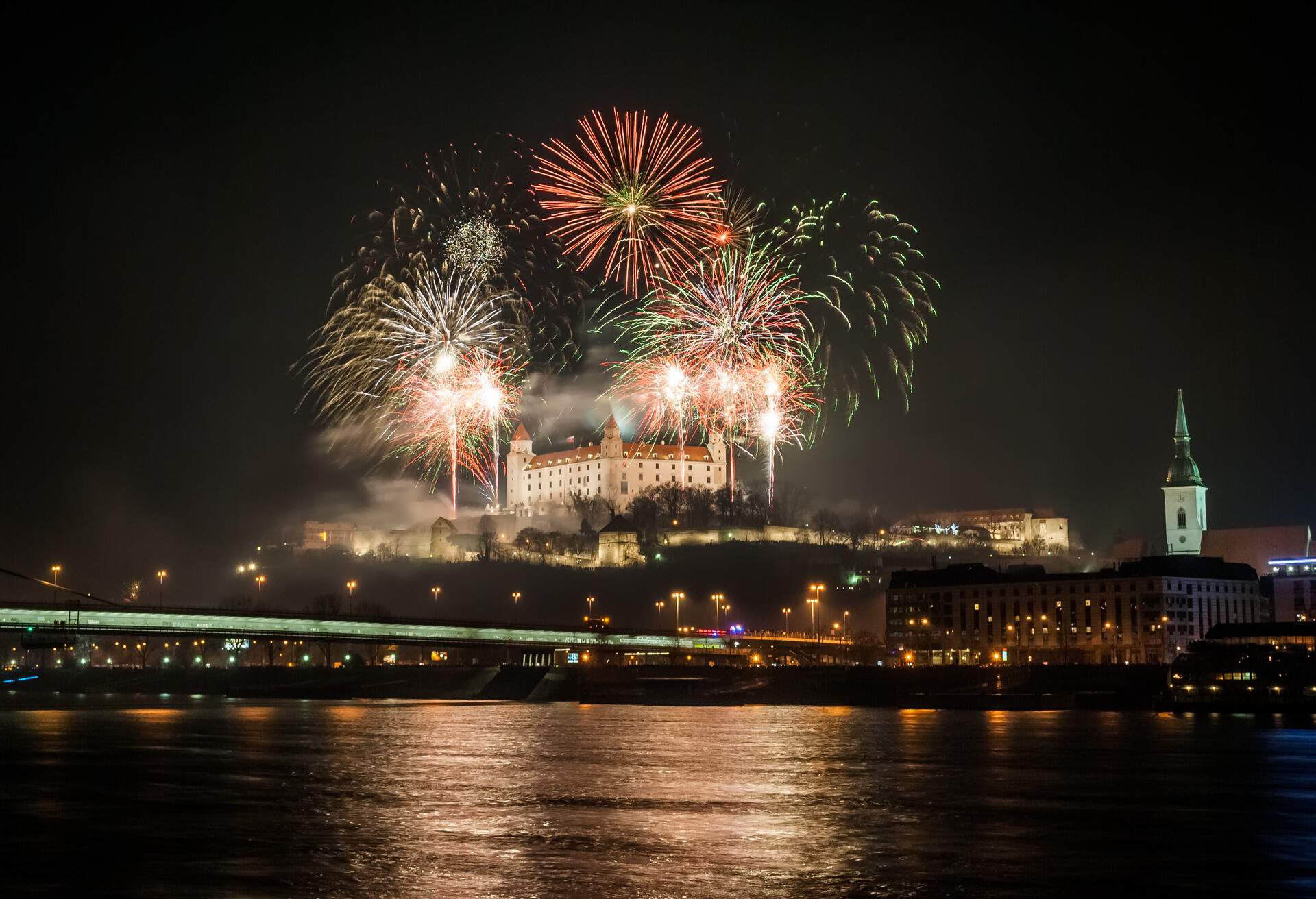 A riverview at night with fireworks and a castle in the middle 