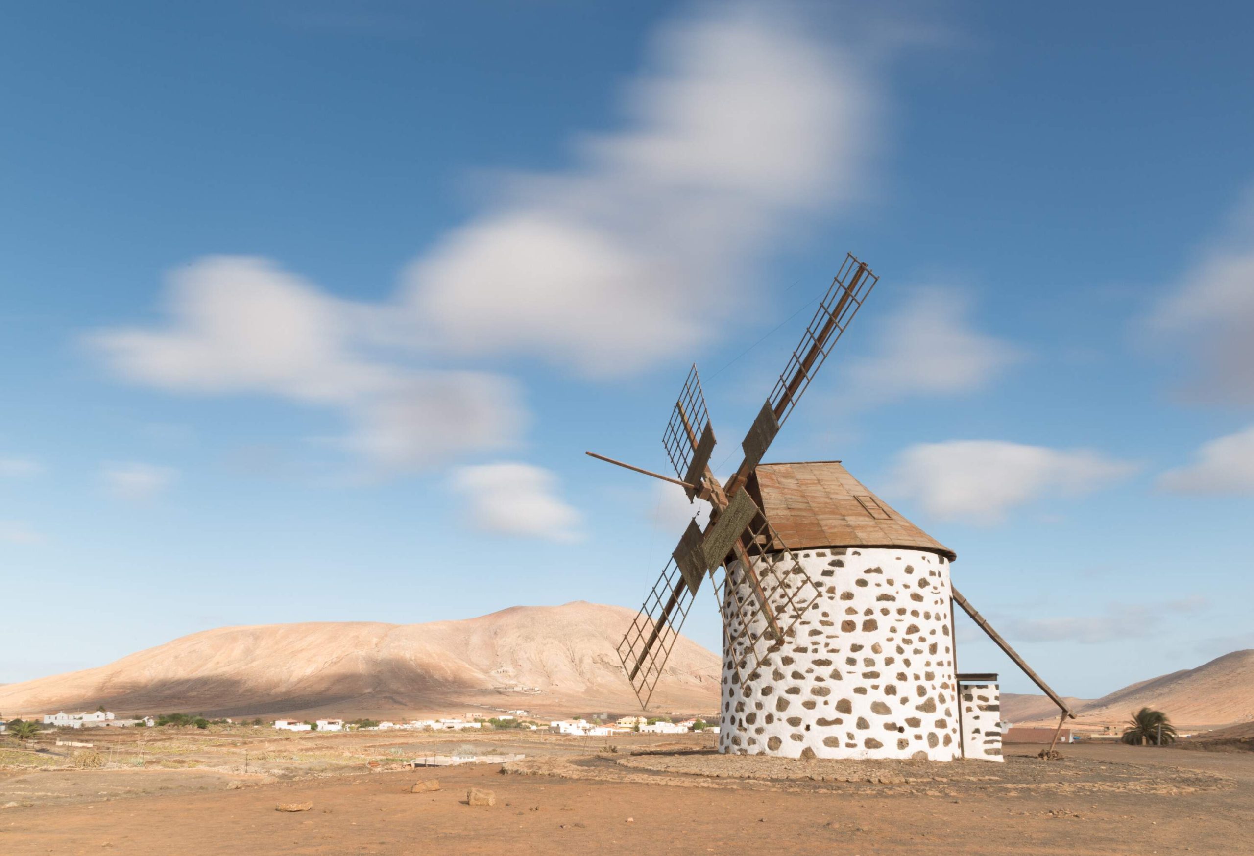 A white cylindrical windmill on a barren field.