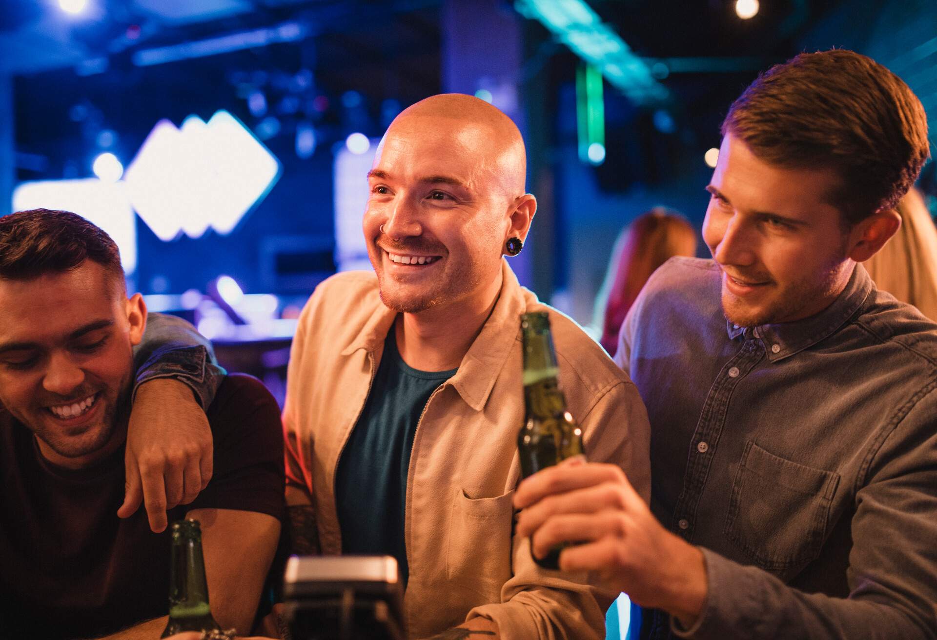 Group of men at the bar with a drink each, they are smiling and laughing at each other.