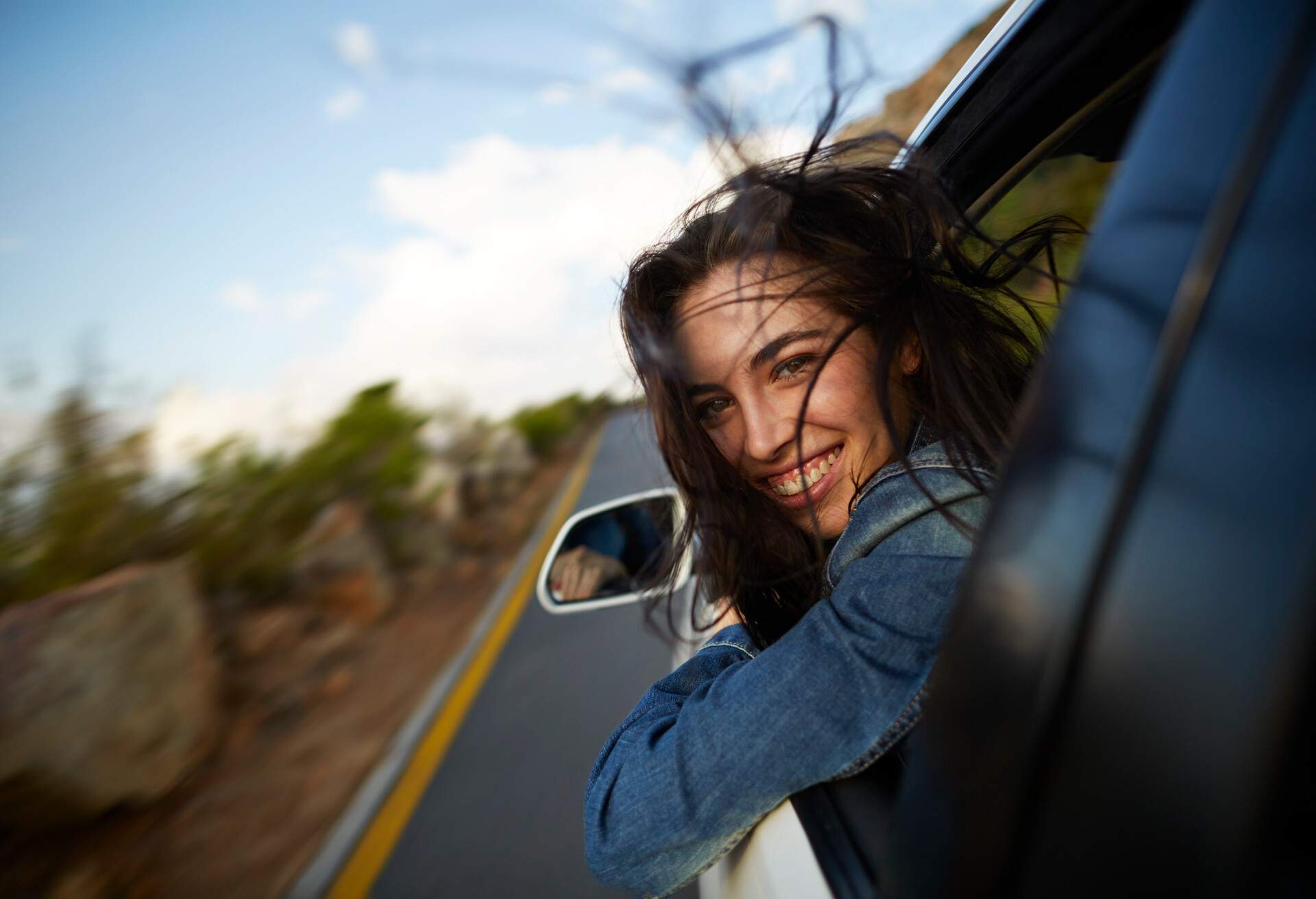 Woman sticking head out of car in motion on mountain road