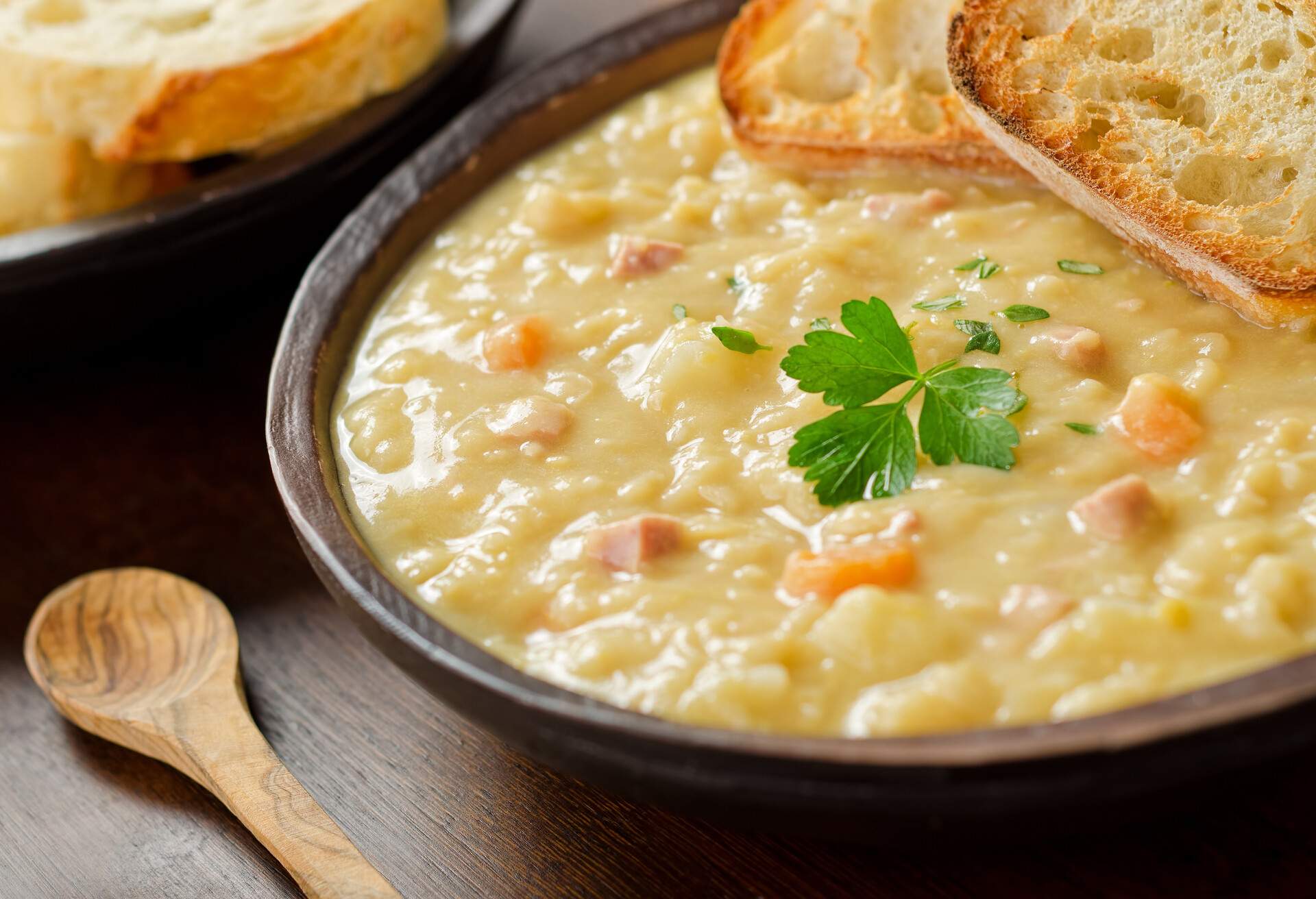A rustic bowl of hearty spit pea soup with smoked ham, carrots, potato, and french bread.