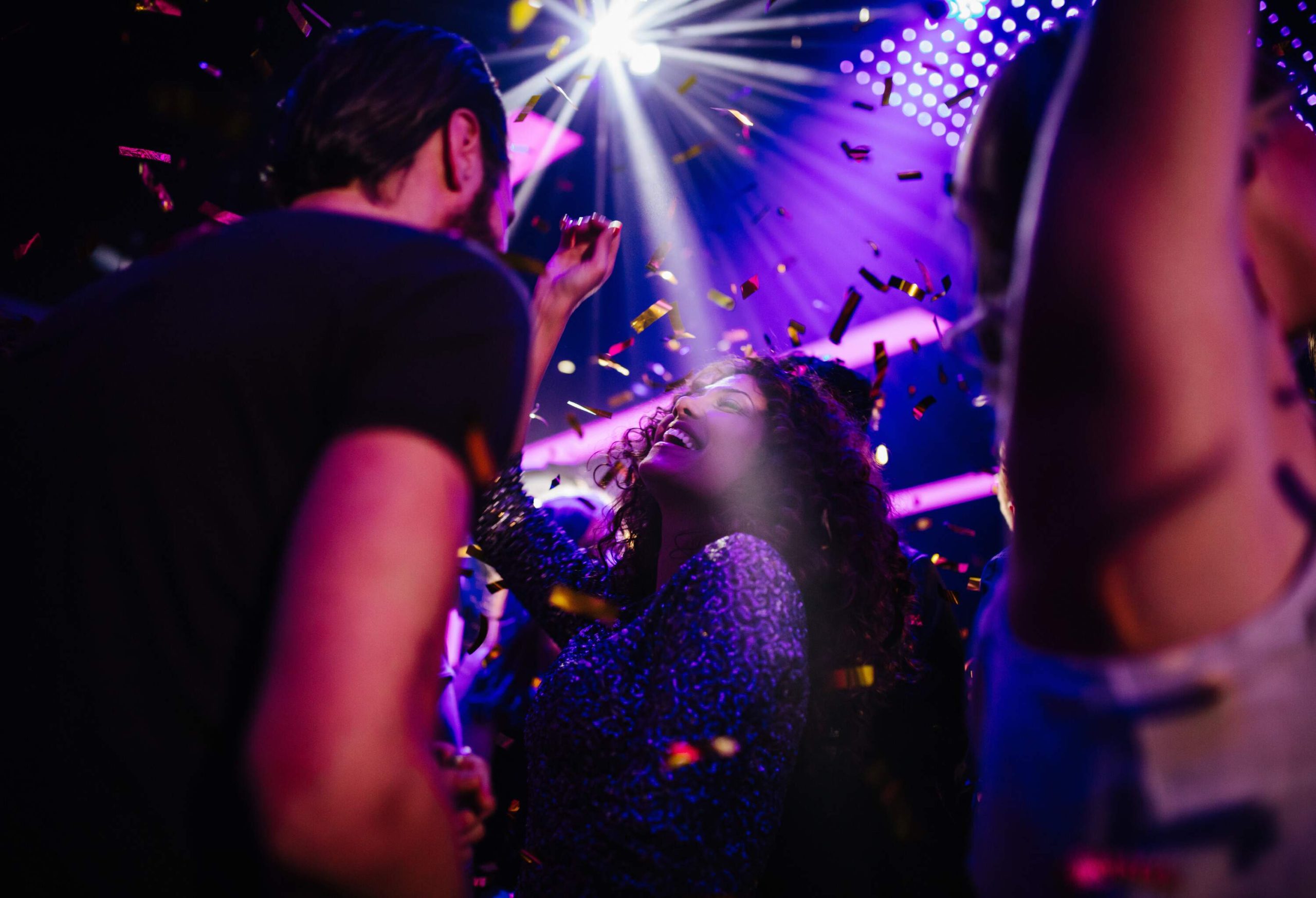 A young, multi-ethnic group of friends joyfully dance and have a blast at a nightclub party, surrounded by colourful confetti as they celebrate life and friendship.