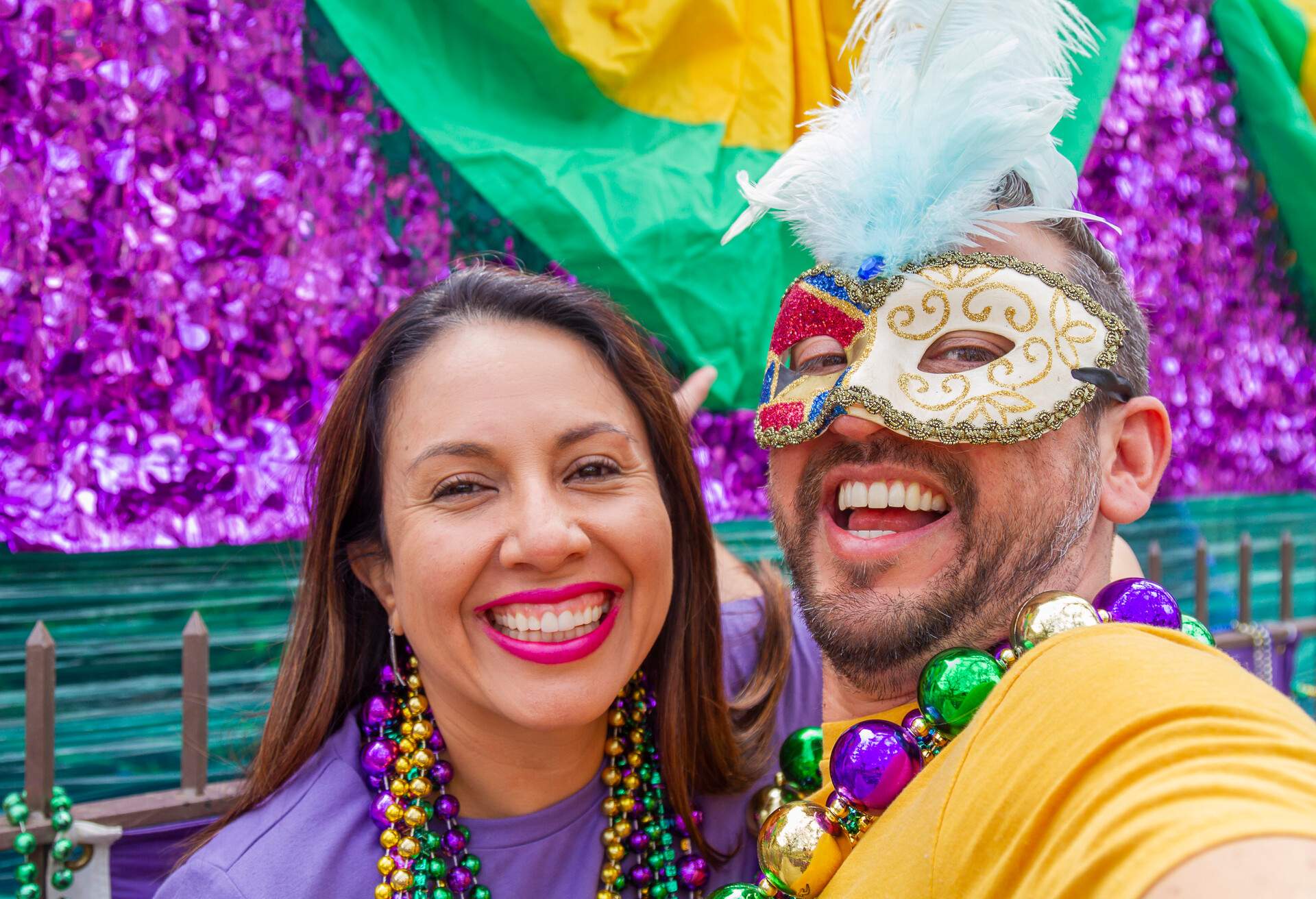 Happy latin tourists friends / heterosexual couple celebrating their Honeymoon in Mardi Gras in New Orleans dressing necklace and masks while taking a selfie. Mardi Gras is the most important celebration for the city.