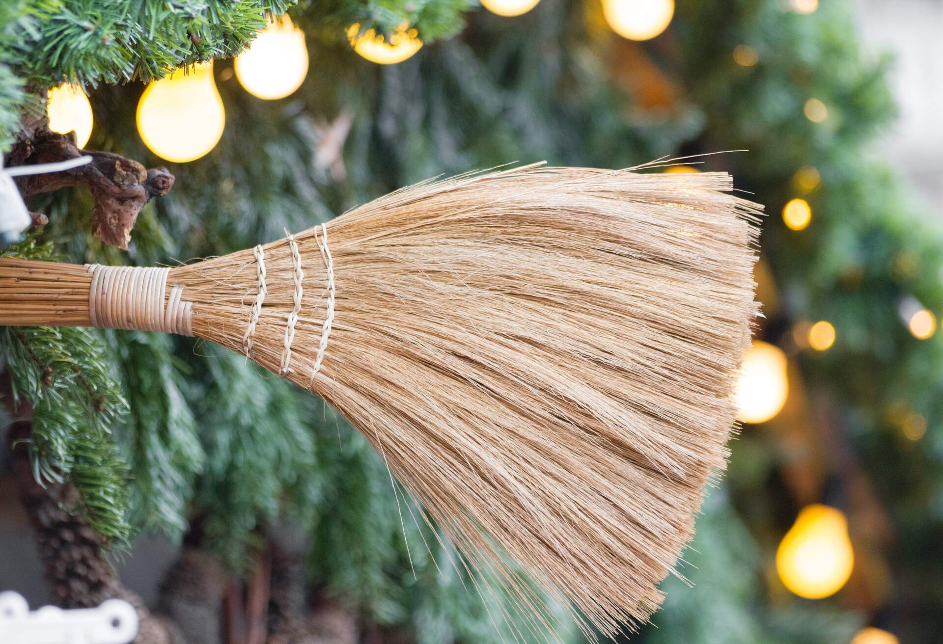 A wooden broom in front of a christmas tree with lights