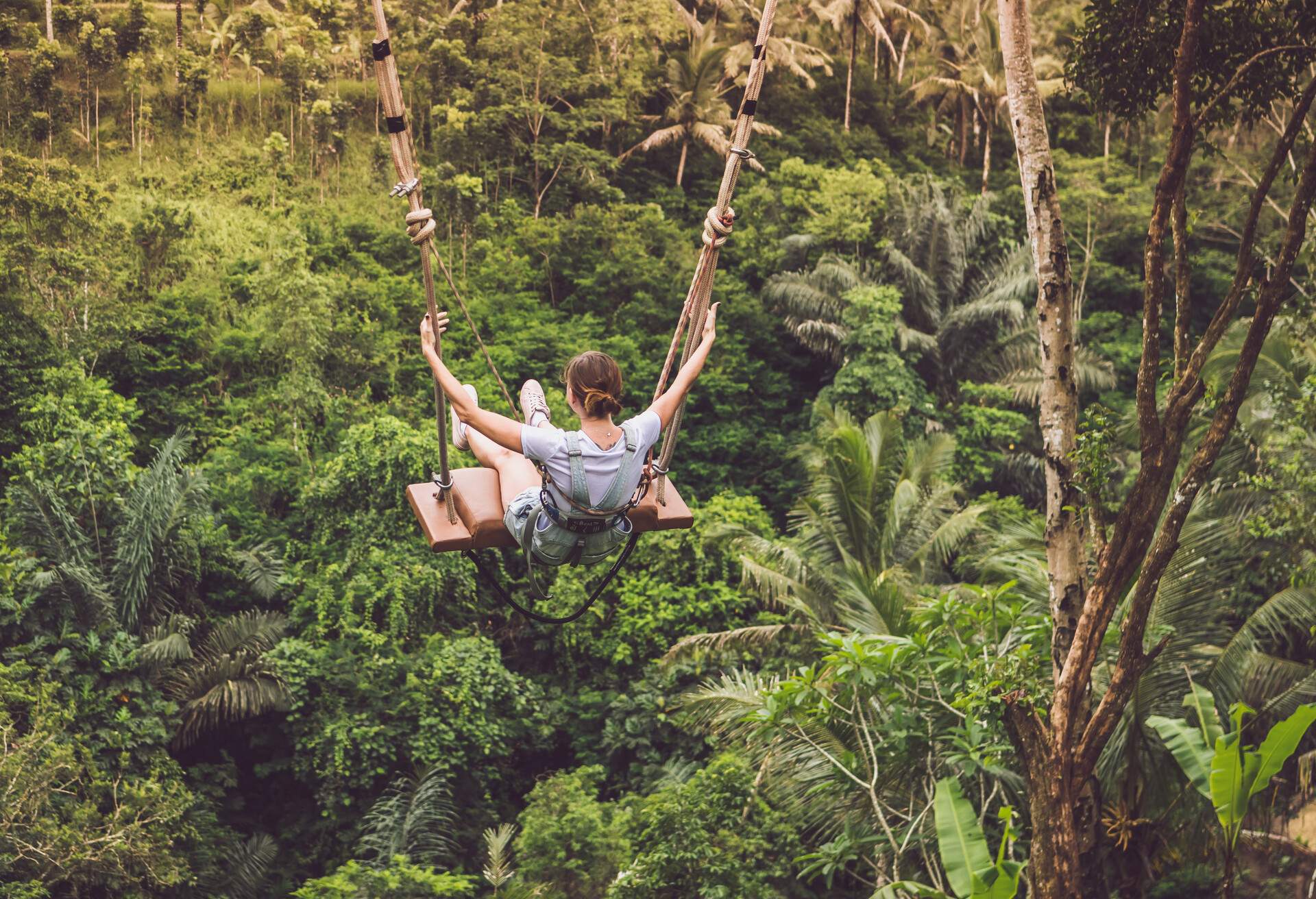 Young tourist woman swinging on the cliff in the jungle rainforest of a tropical Bali island