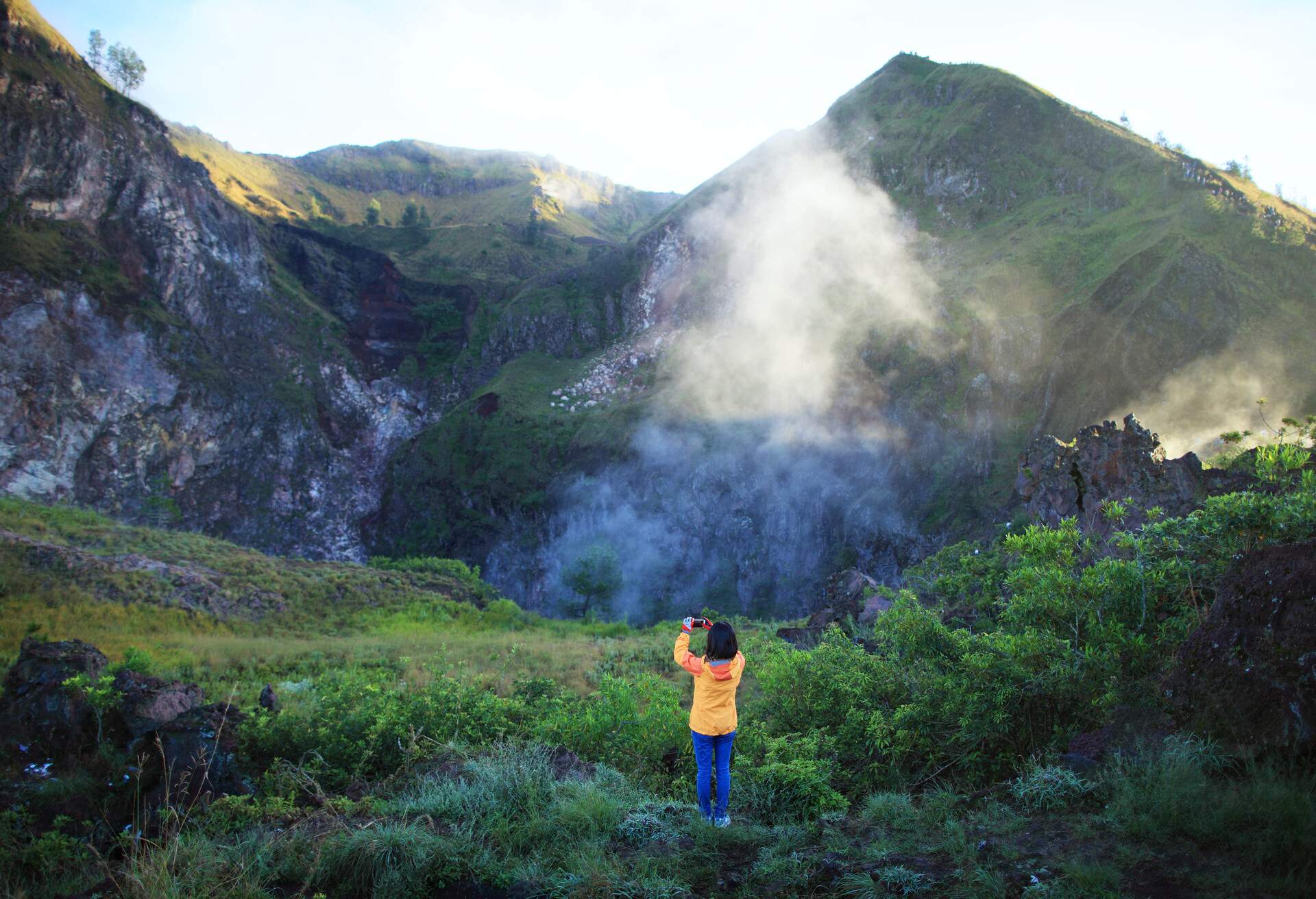 Young woman explorer taking photo with her cell phone in Mount Batur, Bali, Indonesia. 