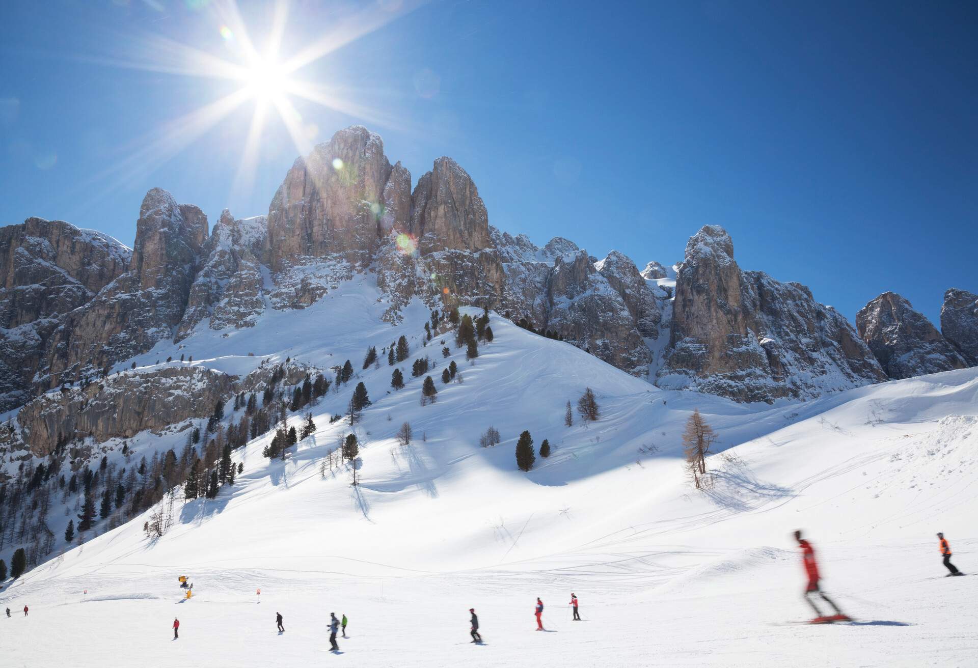 People skiing on a slope backed by a rocky massif in broad daylight.