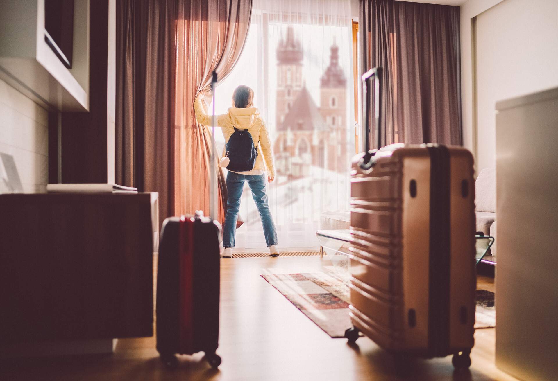 Rear view of tourist in the hotel room pulling the curtains to see the view