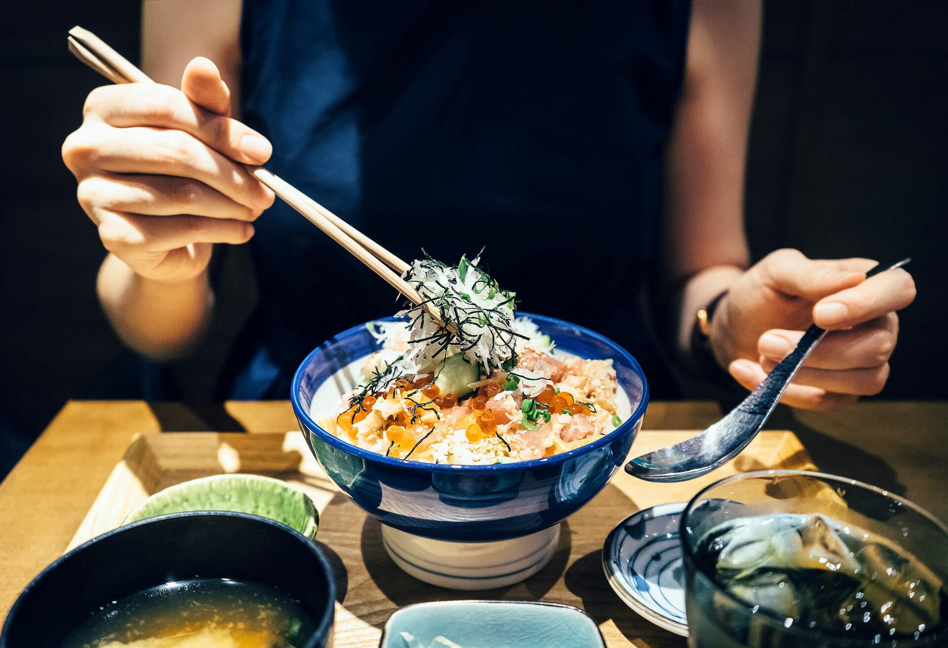 Close up of woman enjoying freshly served traditional Japanese seafood donburi with chopsticks