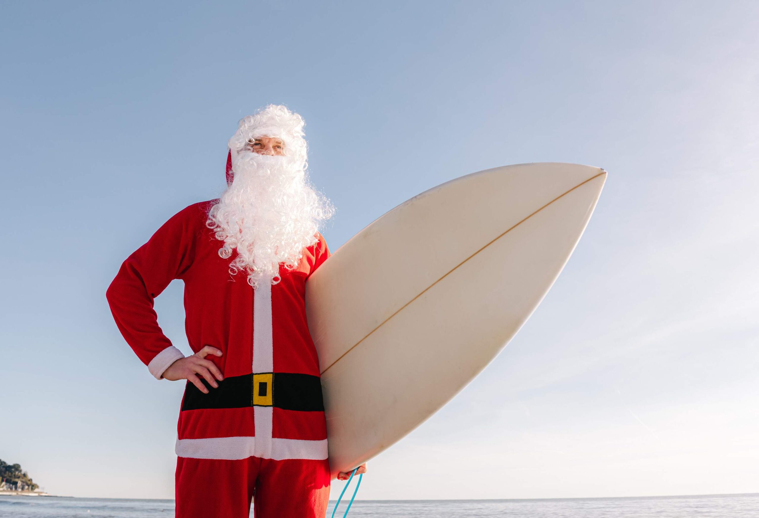 A man dressed as Santa Claus with a surfborad under his arm