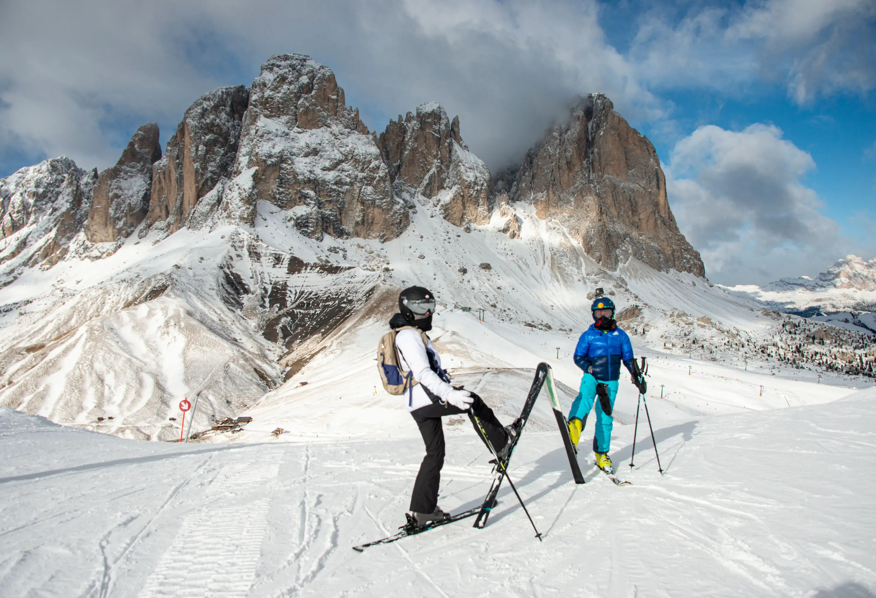 Two skiers pose for a photo with steep rock mountains in the background.