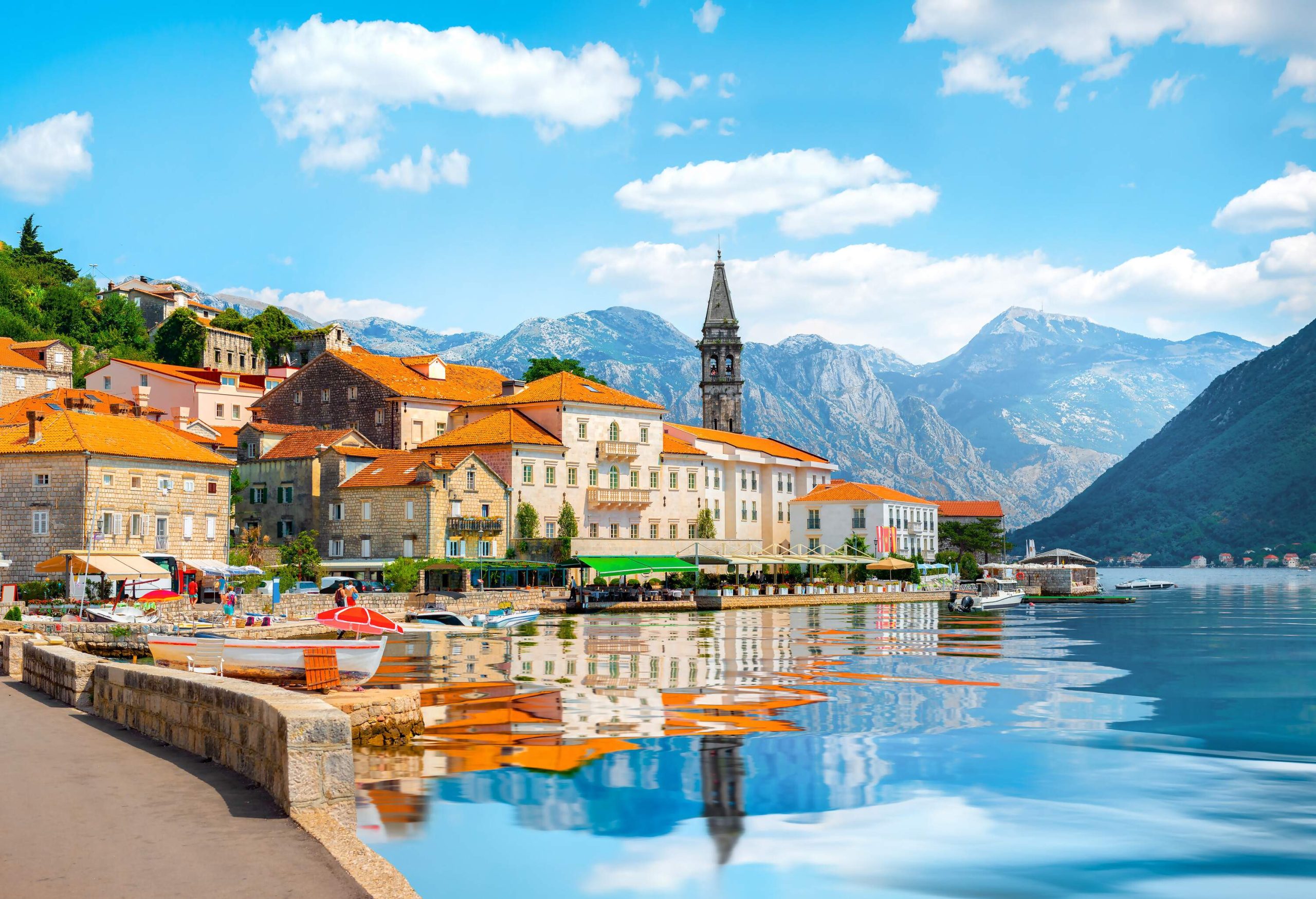 A serene bay reflects the image of a pointed tower and a cluster of waterfront buildings.