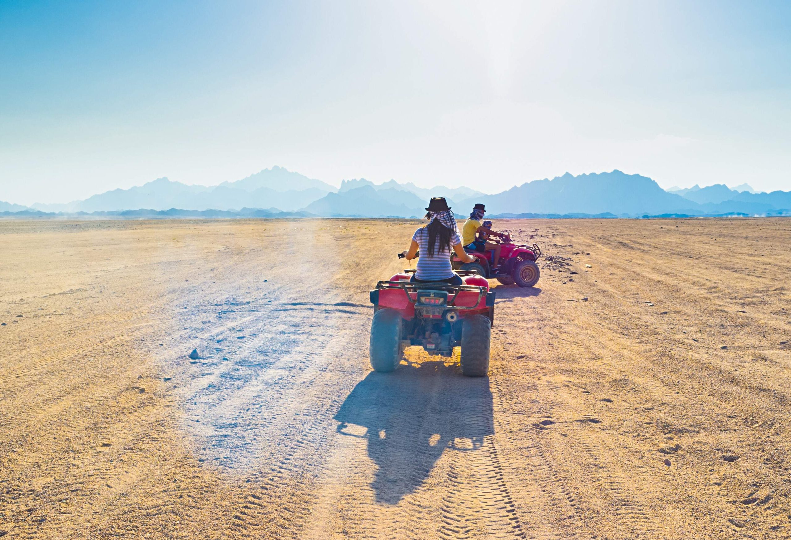 Tourists ride on quad bikes, traversing through a vast desert landscape.