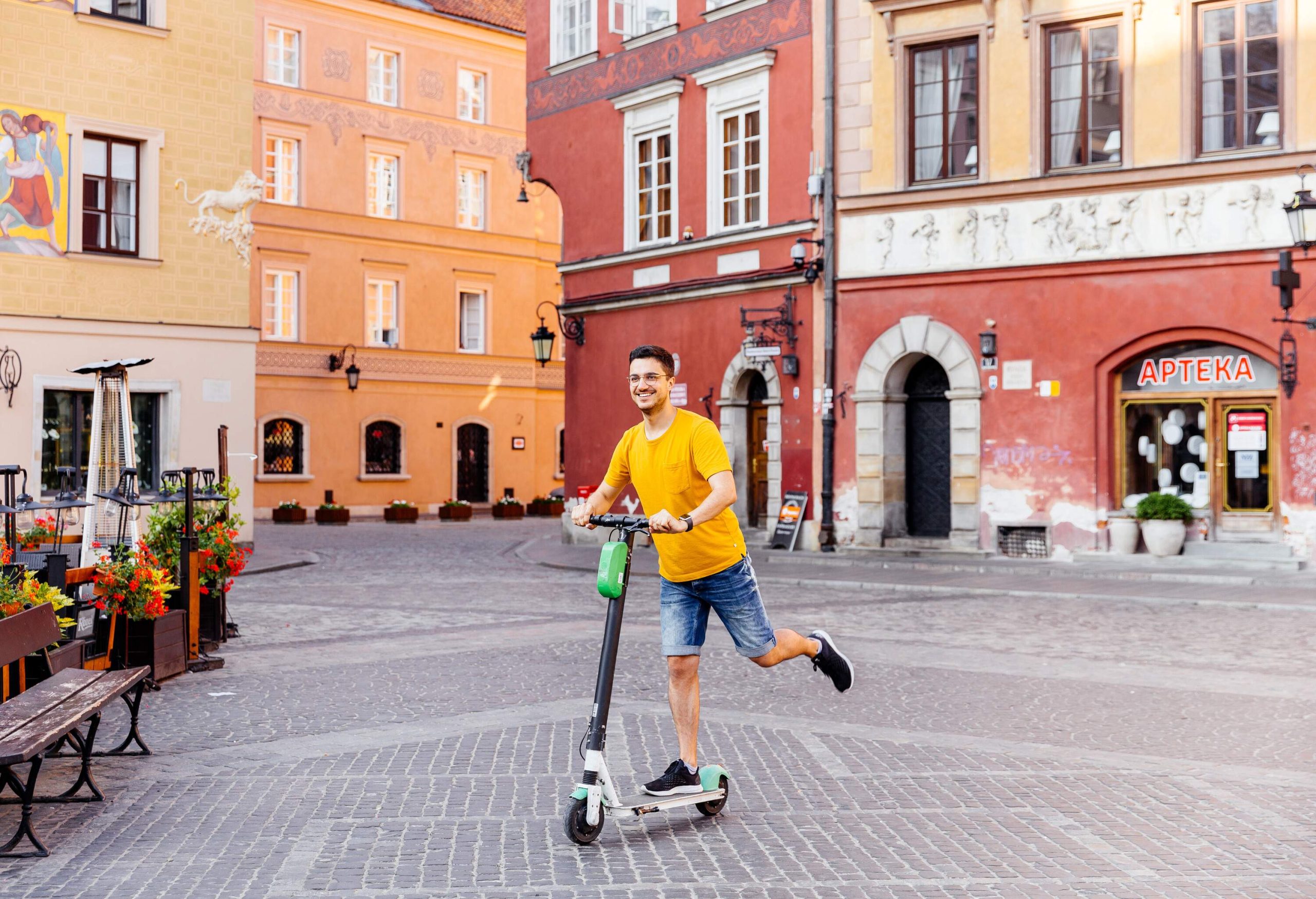 A man rides a scooter in a cobbled square along colourful buildings.