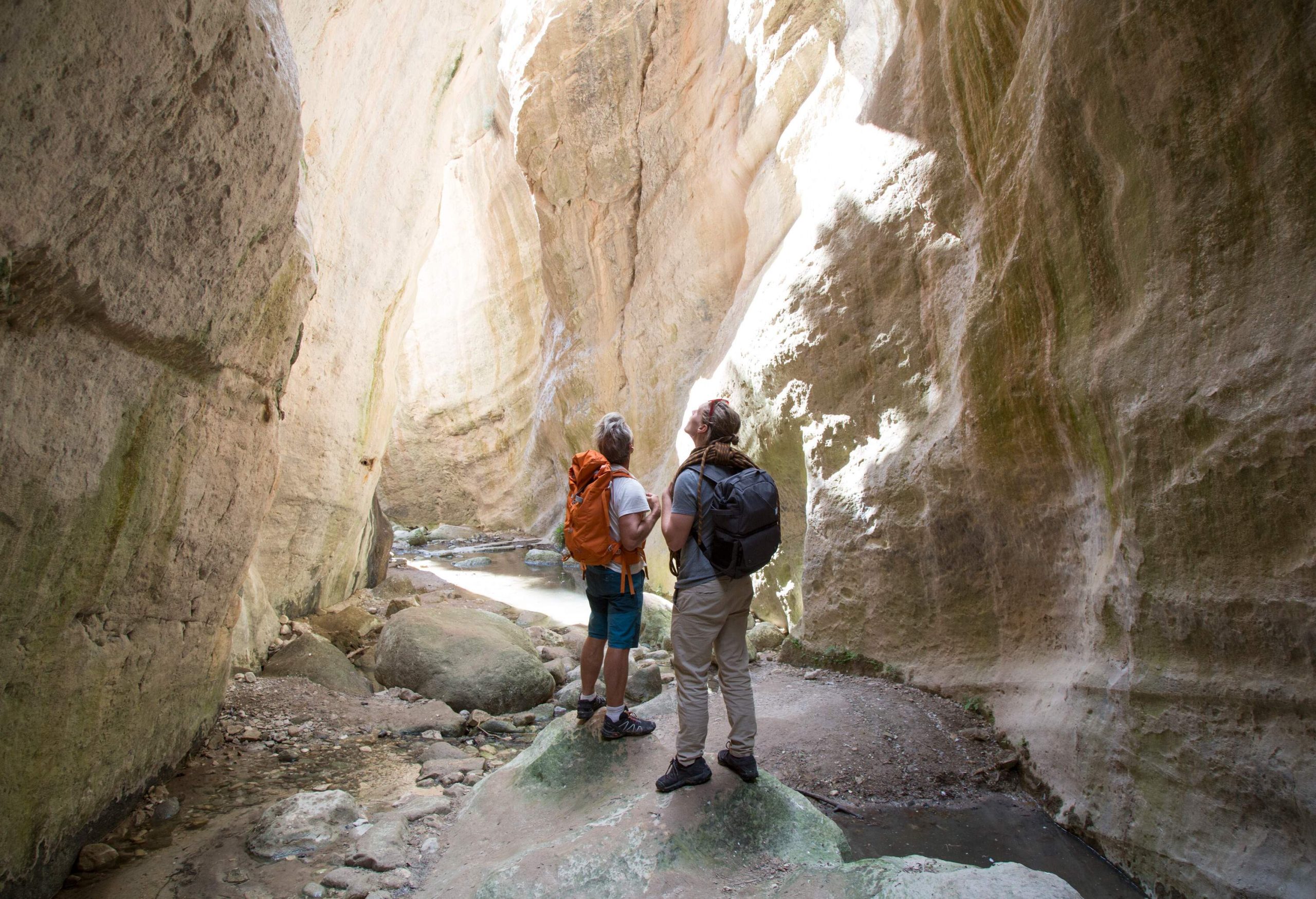 Two male backpackers looking up as they stand inside the gap of rock canyons.
