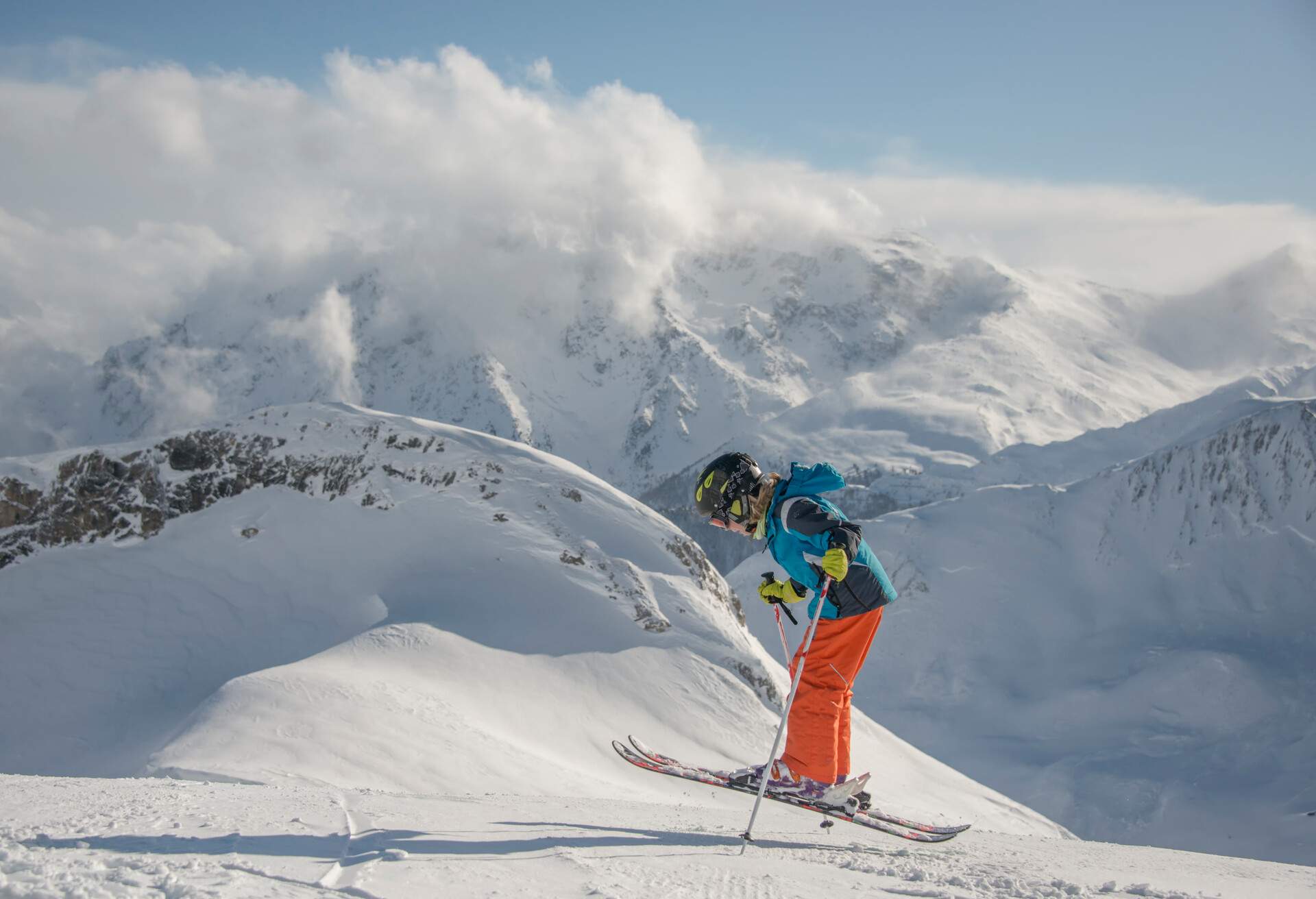 A person wearing ski gear and clutching a ski pole jumps on a snowfield.