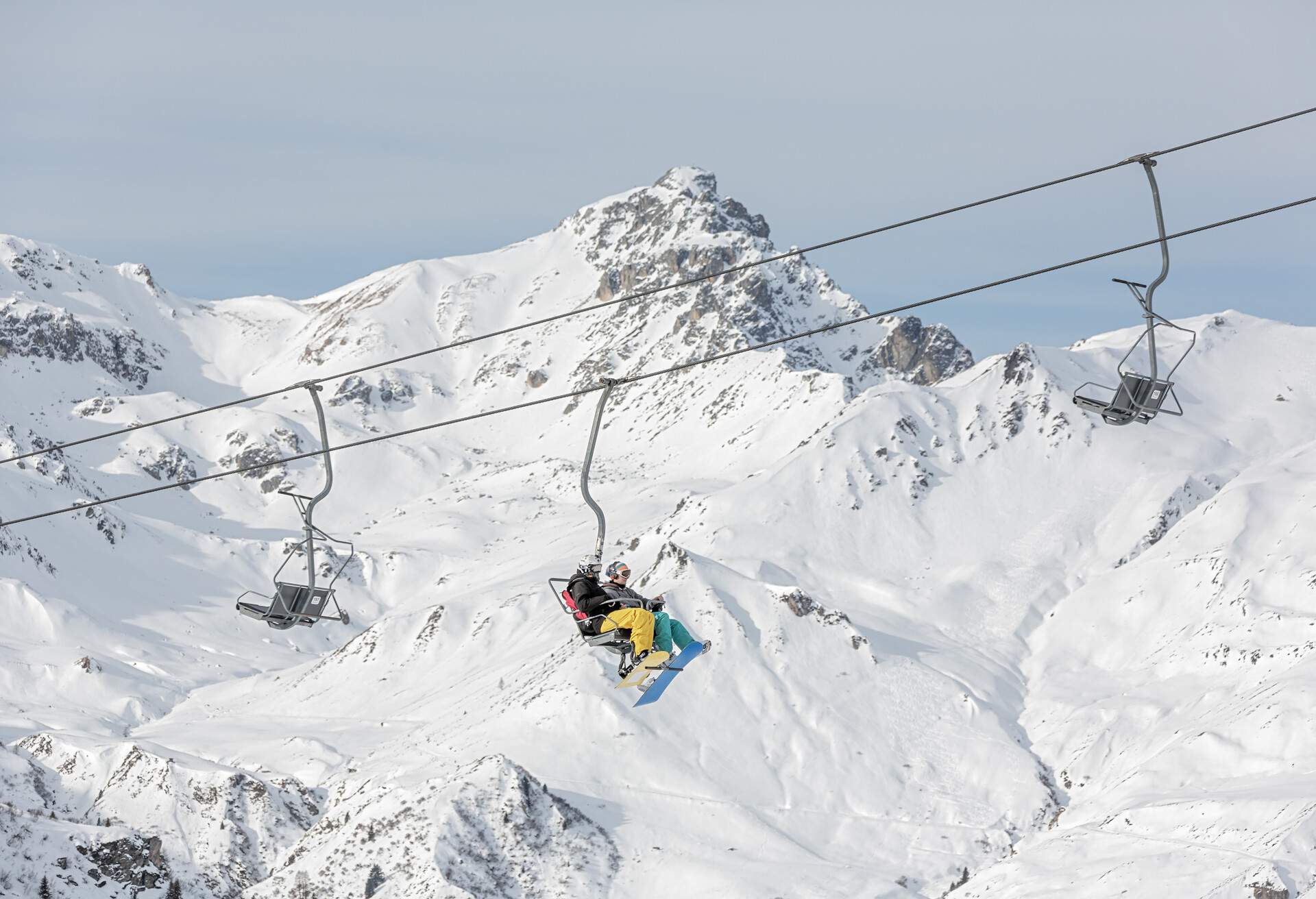 A pair travelling across the snow-covered mountains on a chairlift.
