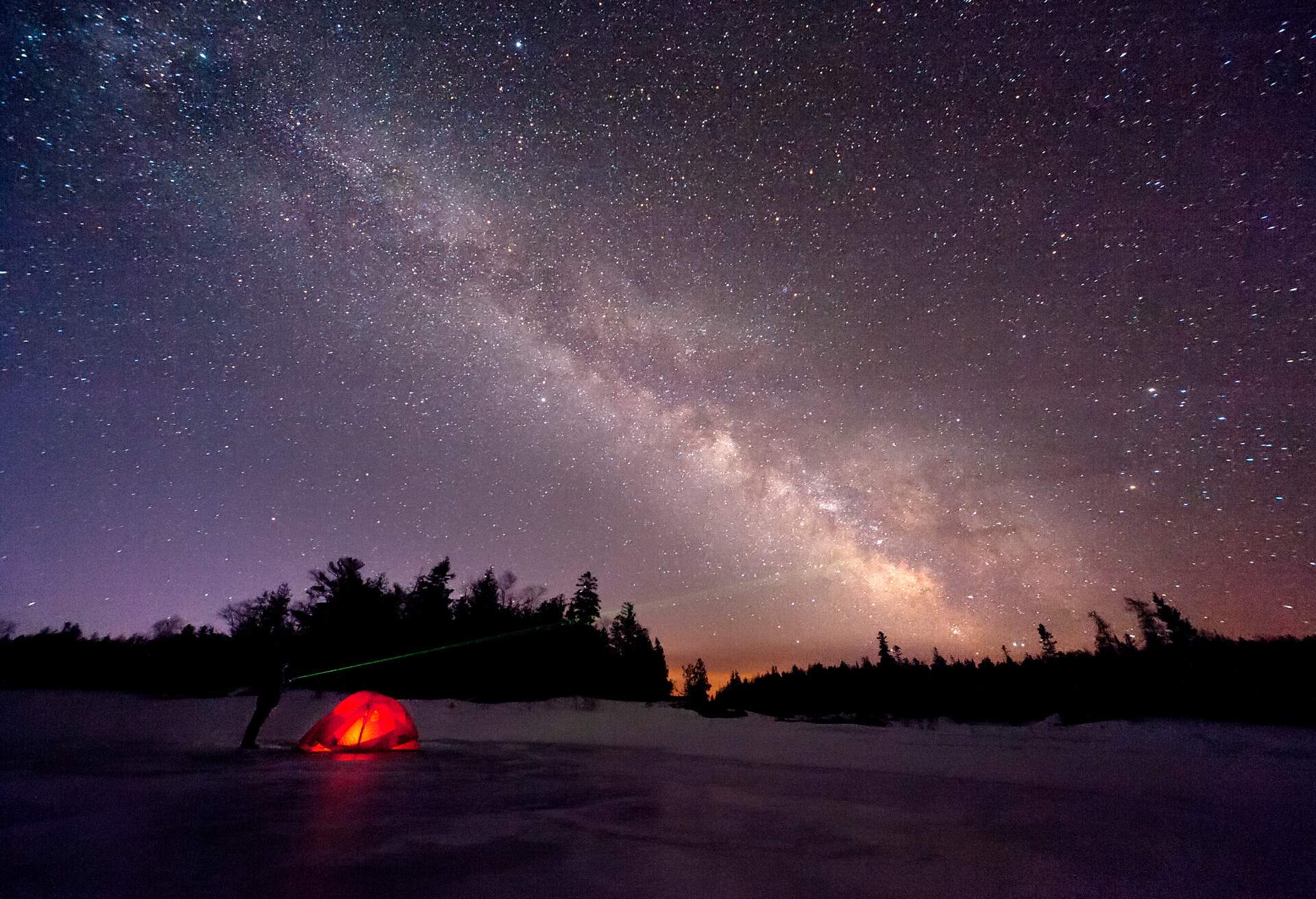 An orange tent glows at night under the constellation of stars.