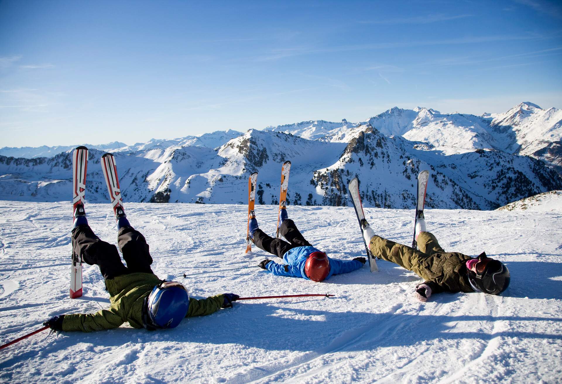 Three skiers with their ski fix, lying down in powder snow land overlooking the rocky mountains covered in snow.