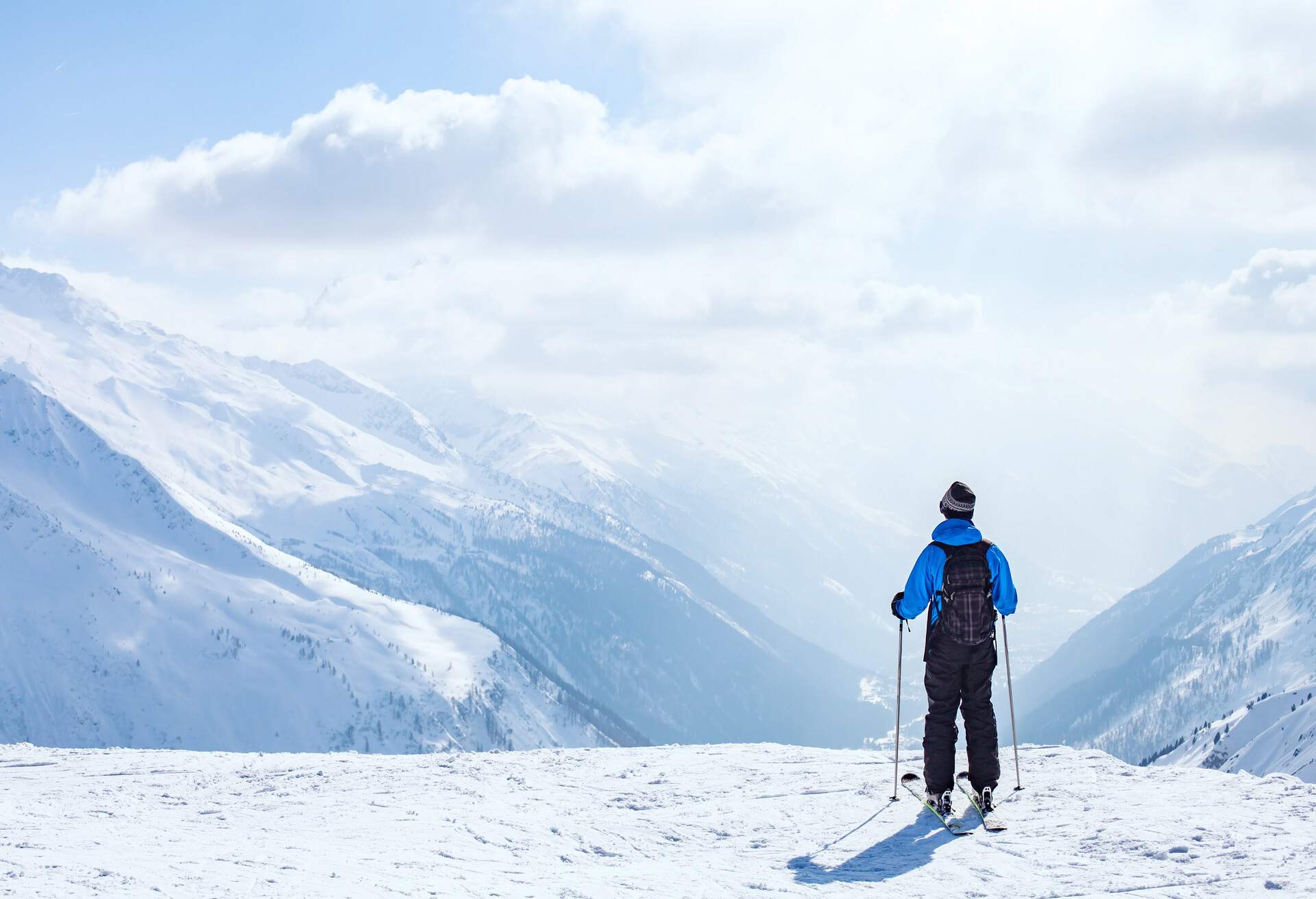Skier with a pole standing on a cliff's edge and appreciating the snow-covered mountains.