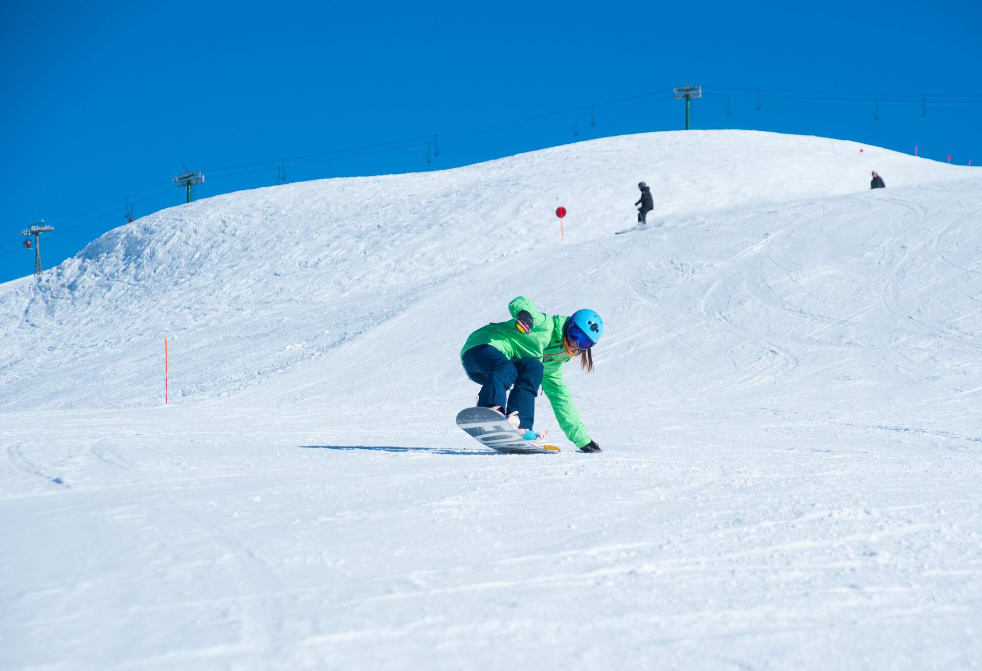 A snowboarder in a green winter jacket and ski helmet is snowboarding down a sloppy snowfield of a mountain.