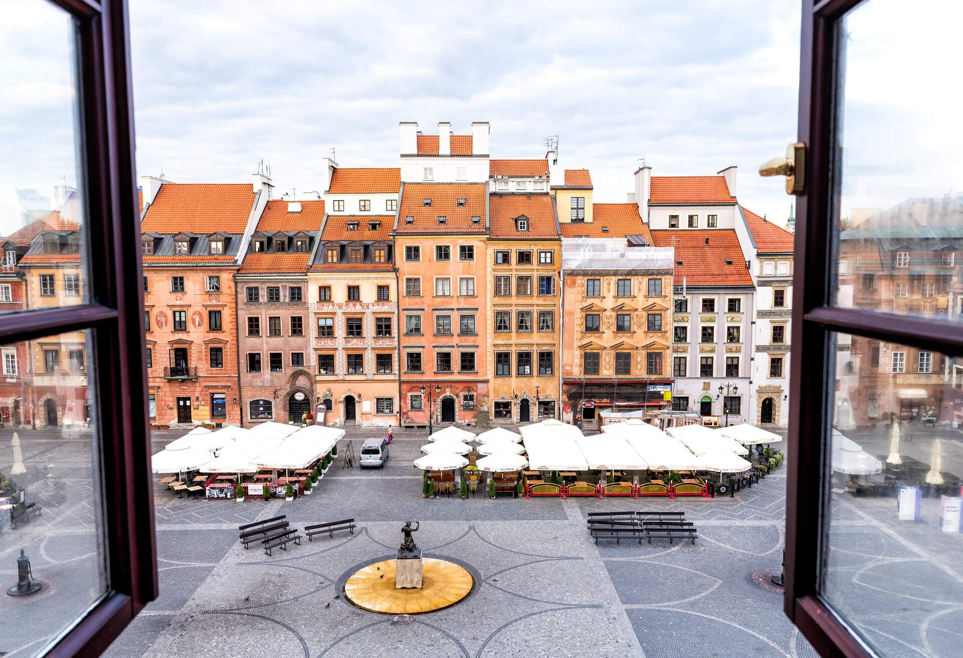 Historic cityscape with view through open glass window of colorful architecture buildings in old town market square in empty morning with fountain in Warsaw, Poland