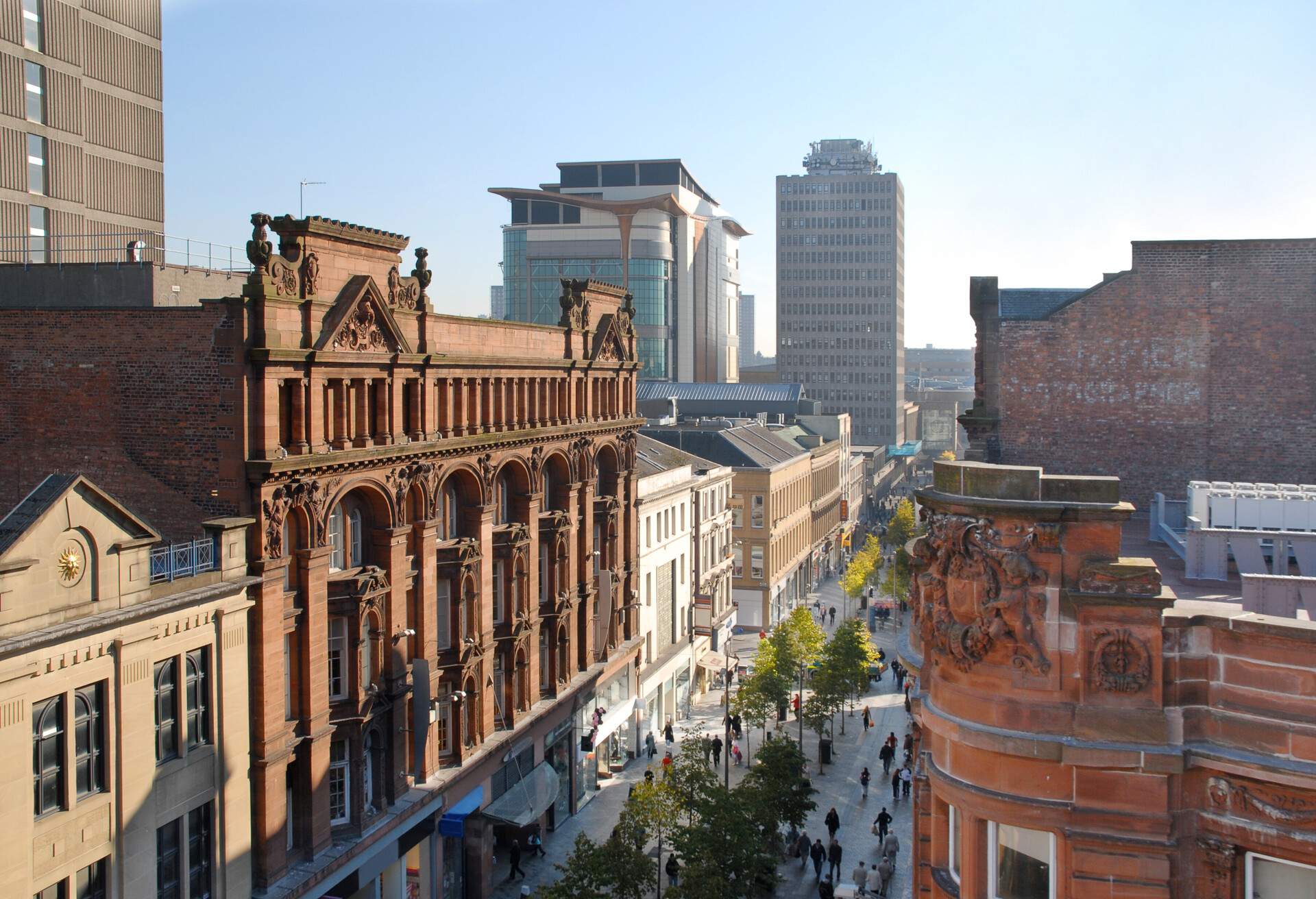 A crowded tree-lined street bordered with adjacent buildings with intricately designed façades.