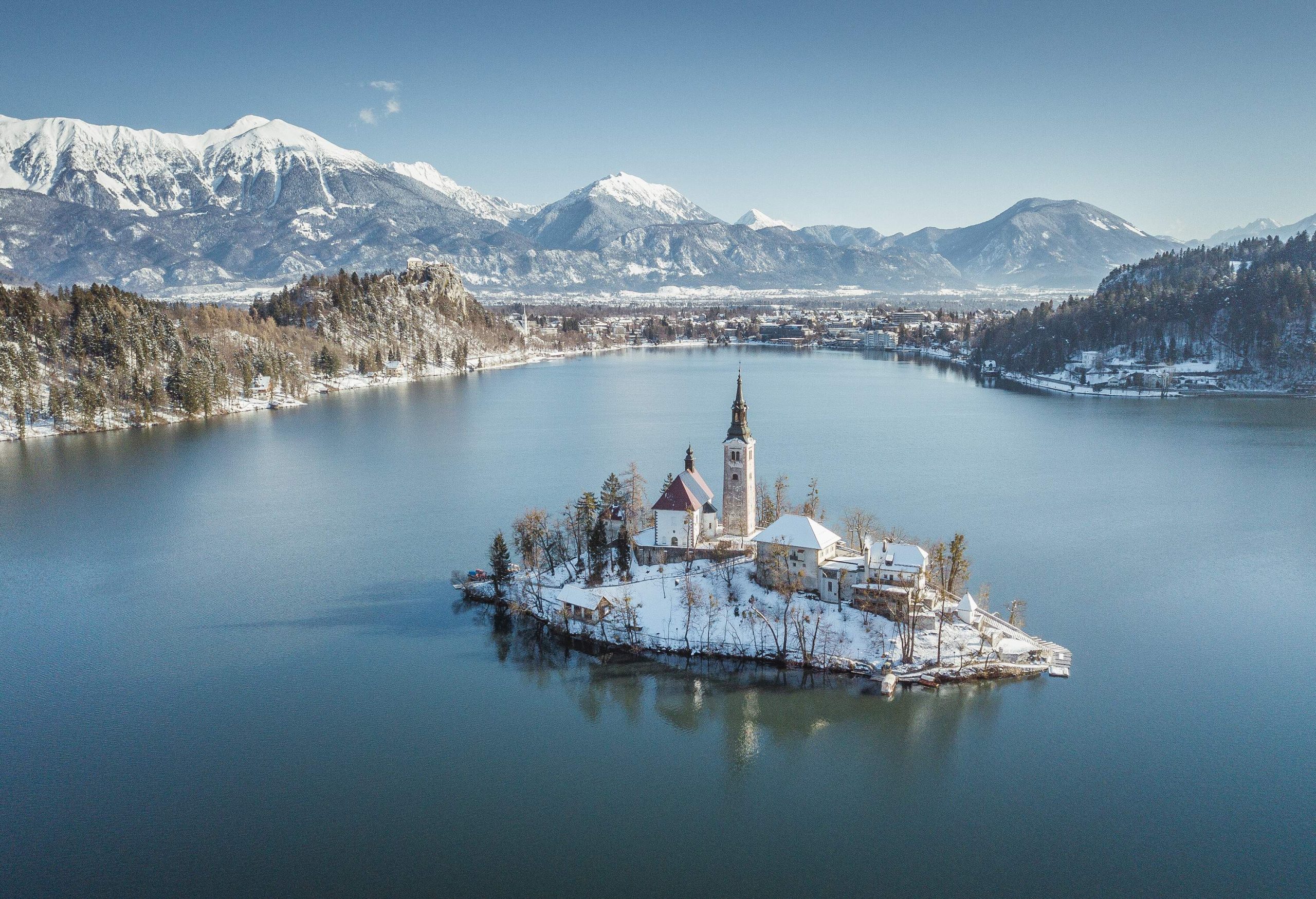 Panoramic view of famous Bled Island (Blejski otok) at scenic Lake Bled with Bled Castle (Blejski grad) and Julian Alps in the background on a beautiful sunny day in winter, Slovenia