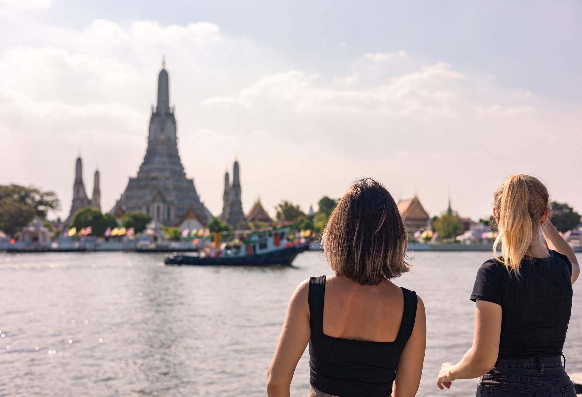 Two women gaze at the passenger boats on the river and the Wat Arun temple in the distance.