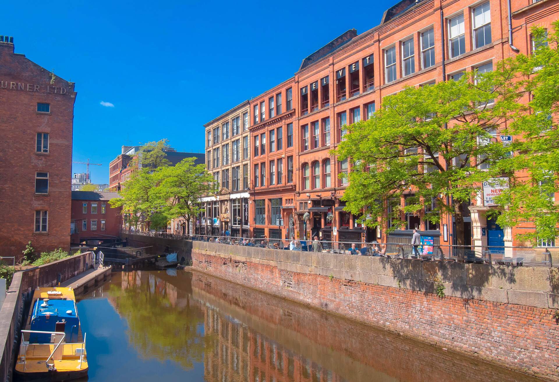 Adjacent buildings with outdoor seats and tables along a canal with a docked boat.