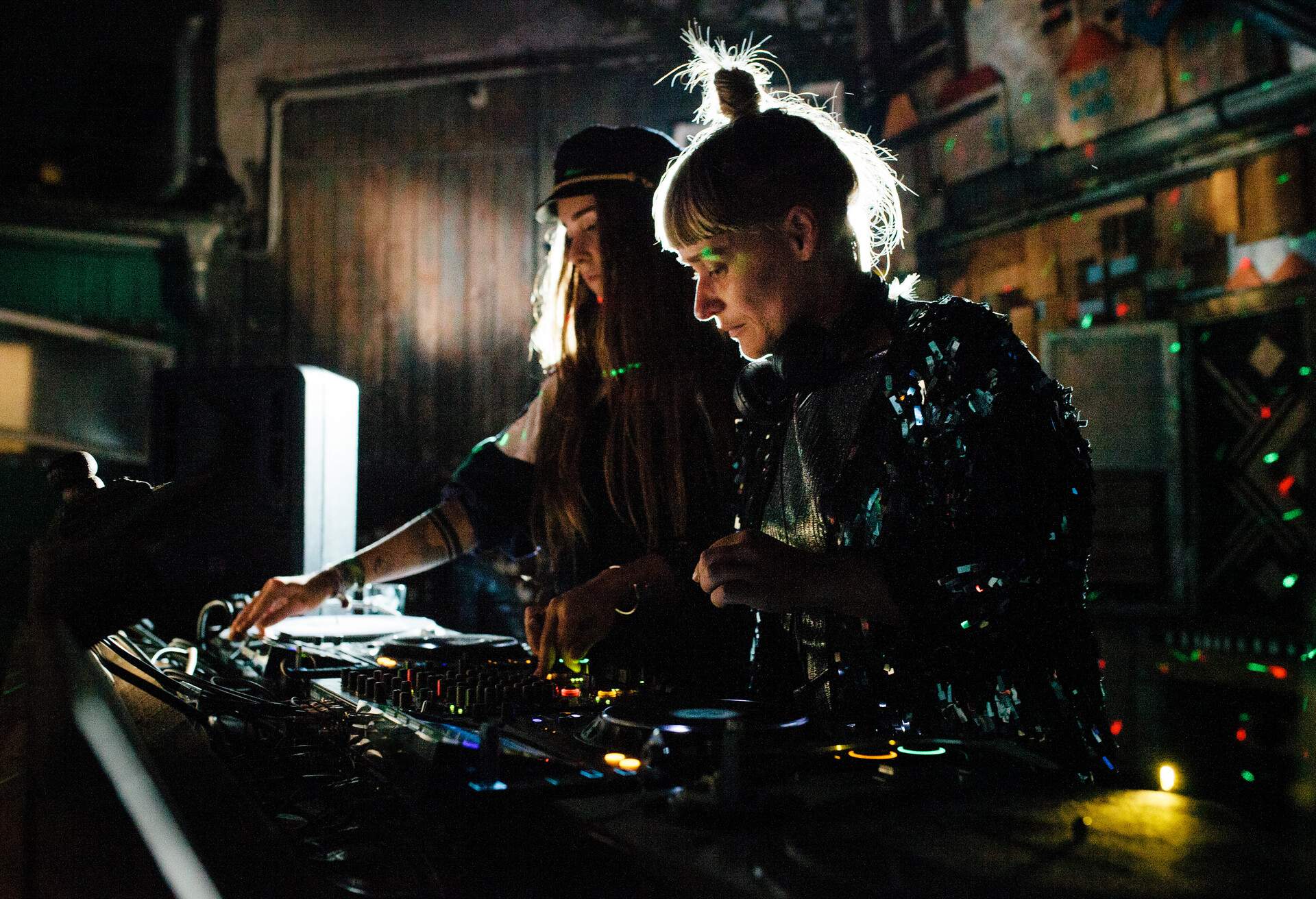 Two DJs in party attire are busy playing with the controllers at a club.