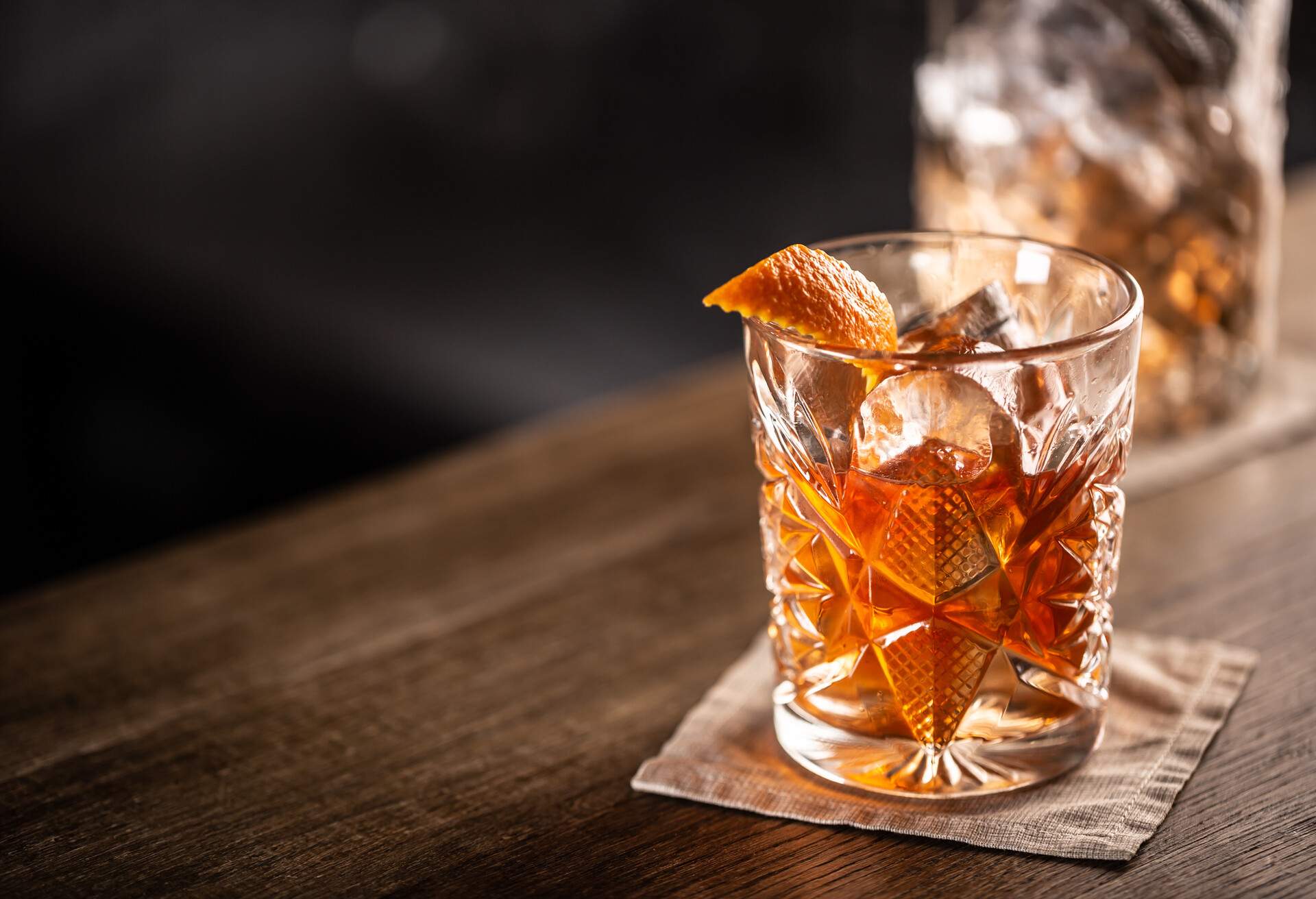 Old fashioned whiskey drink on ice with orange zest garnish.