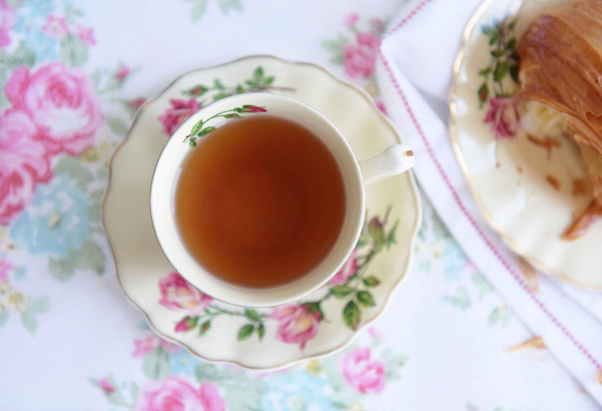 Cup of tea in a vintage rose cup and saucer with a pulled apart fresh pastry.