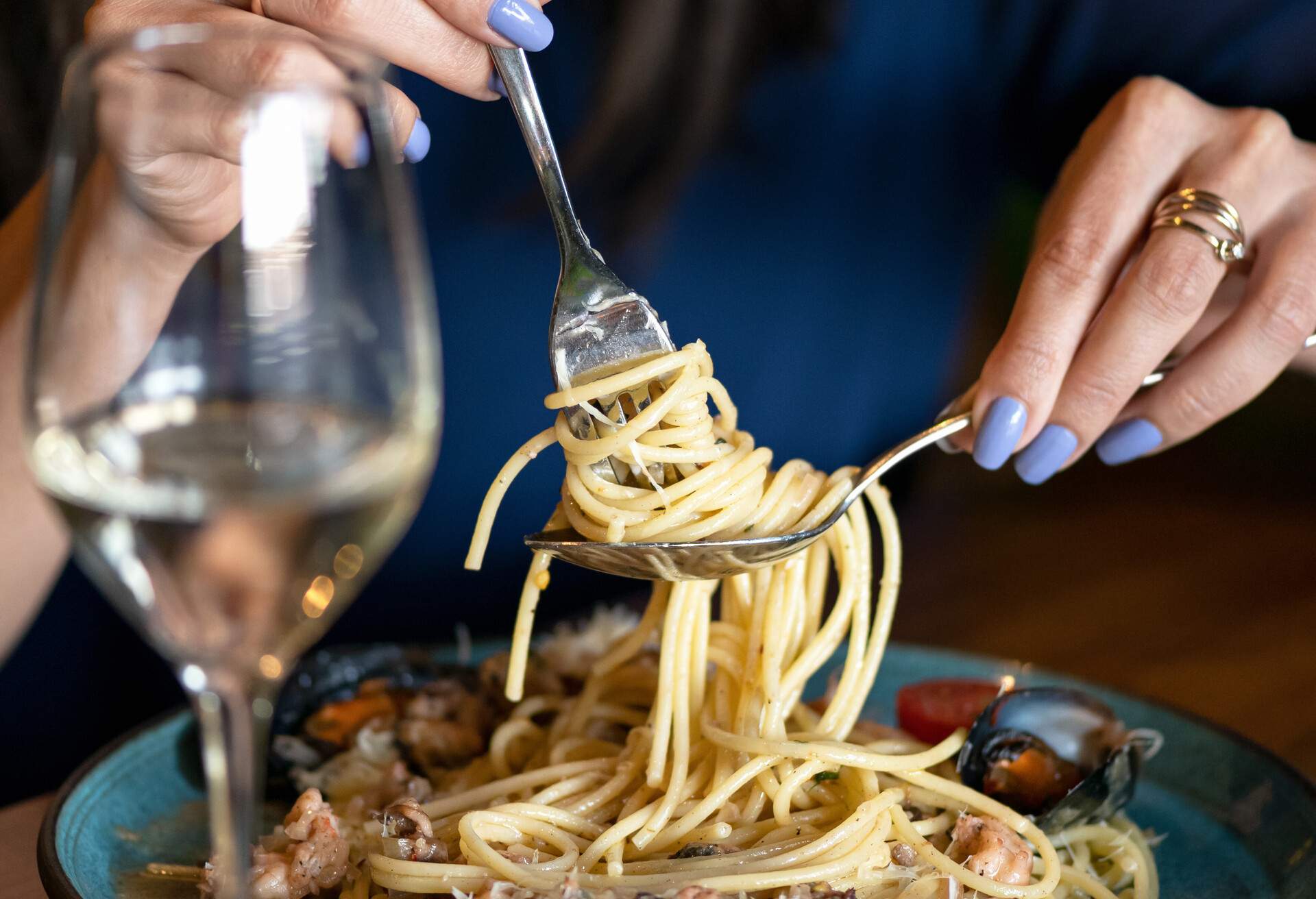 Spaghetti with mussels. Woman winds on fork seafood and Italian pasta. Close up shot. Healthy exotic lunch. Soft focus.