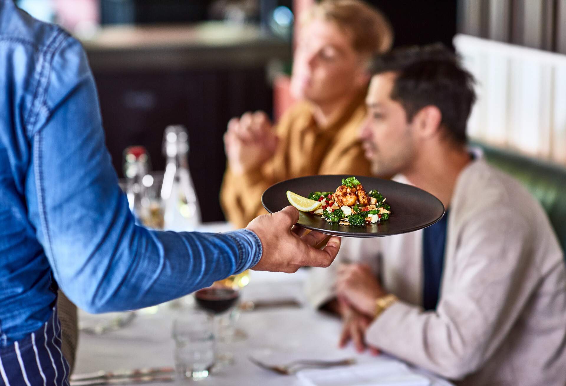 Close up of man holding plate with gourmet food, serving people at table in restaurant