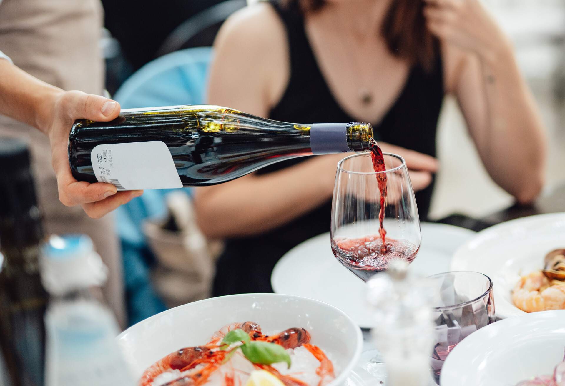 Close-up of a male hand pouring wine into a glass. Waiter serving red wine at luxury Italian restaurant. Luxury meal. Wine Tasting. Wine pairing.