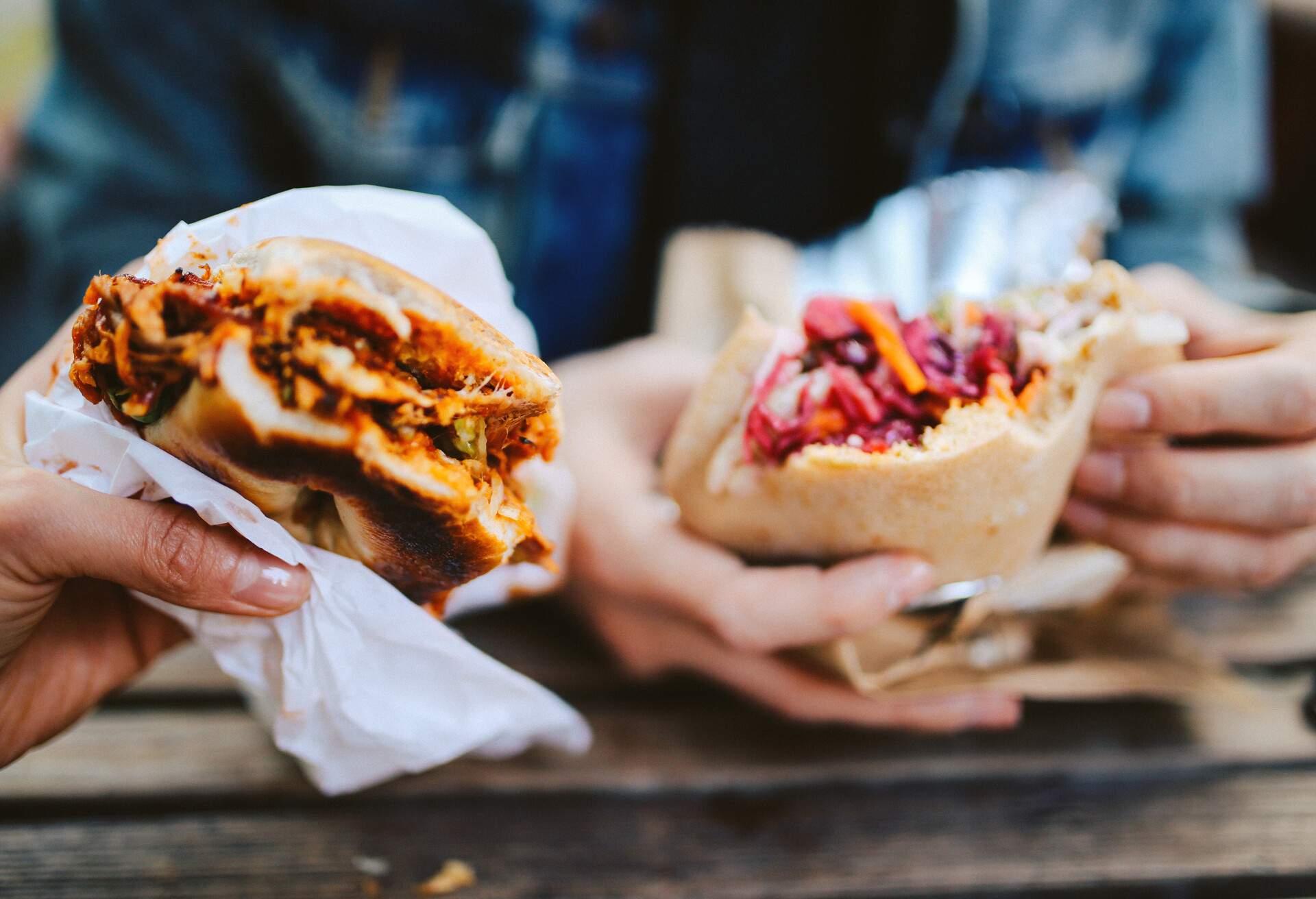 Close up image of two people eating a Texas style pulled pork barbeque and a falafel fast food in East London.