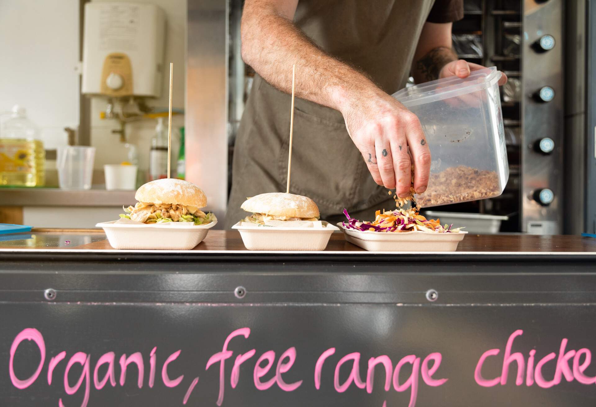 A chef prepares a roast chicken and salad and two chicken burgers on biodegradable plates out of a food truck