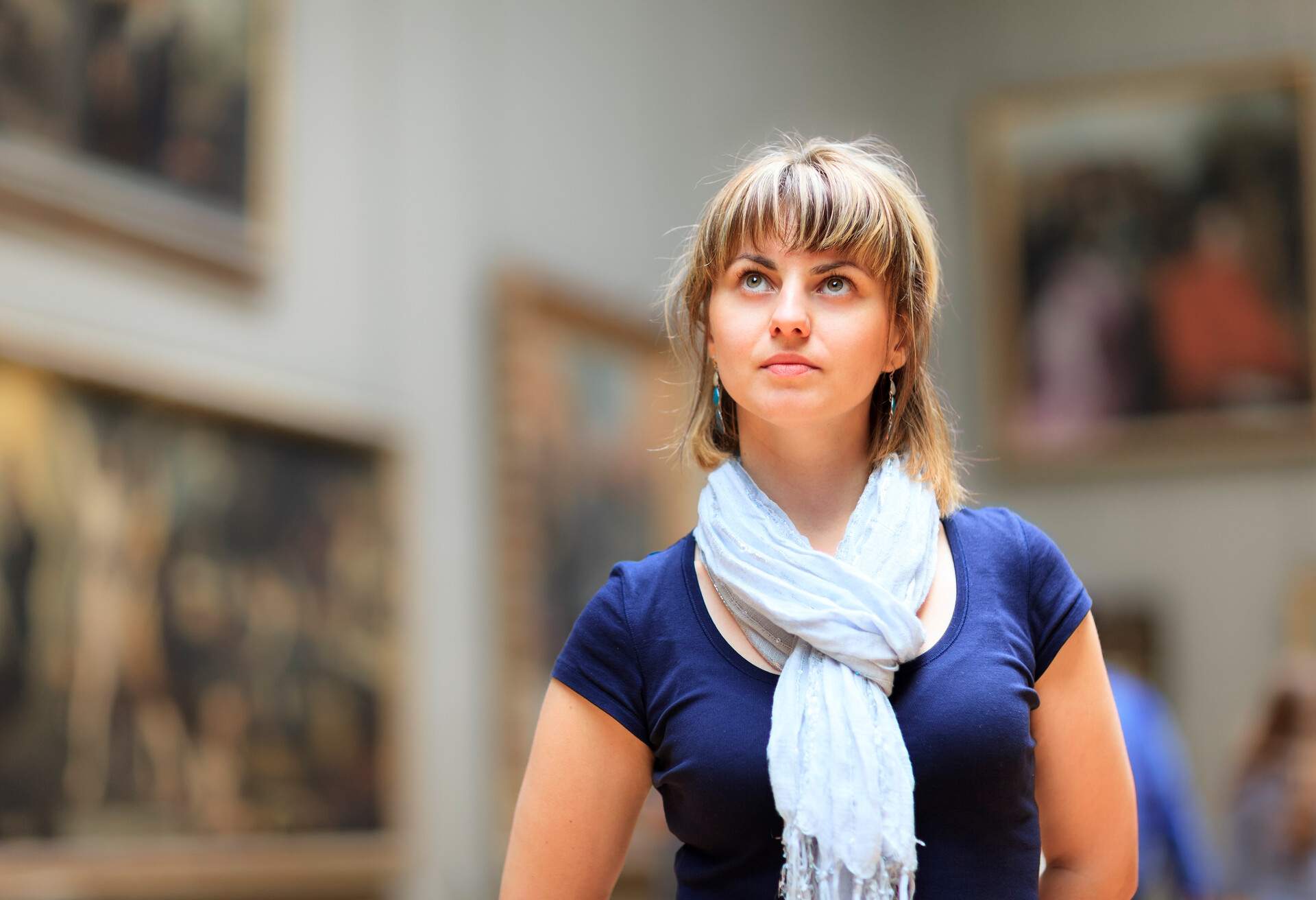 Woman in art museum looking up at paintings.