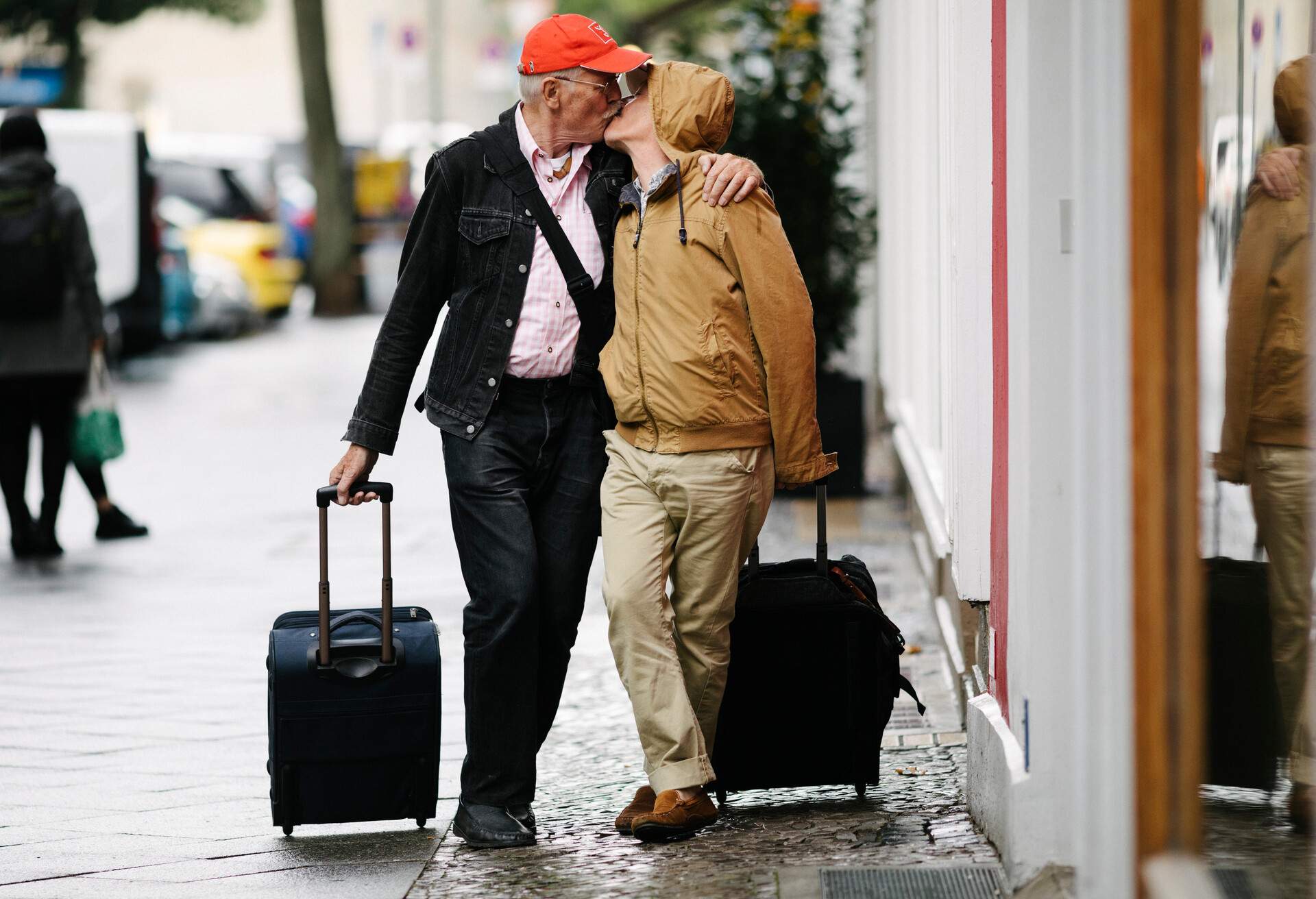 A mature gay couple kissing in the street while walking with their luggage on the way to a hotel together.