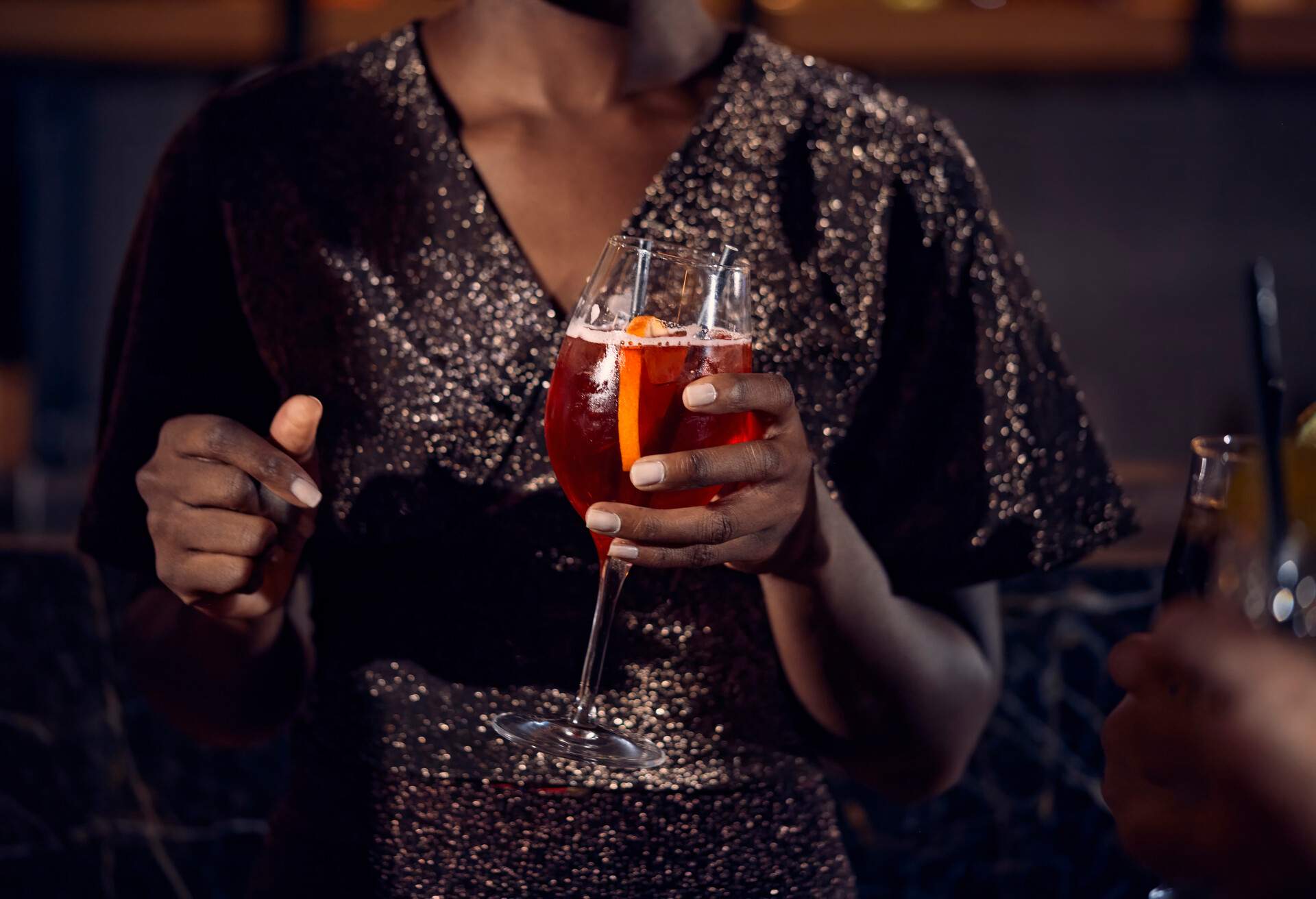 Close-up of a person in a sparkly dress and holding a drink.