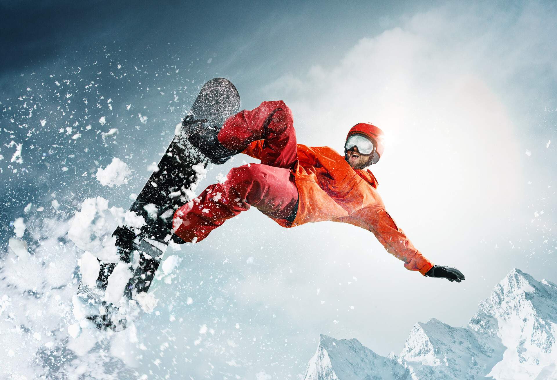 A snowboarder jumping over powder snow and a view of the snowy mountains.