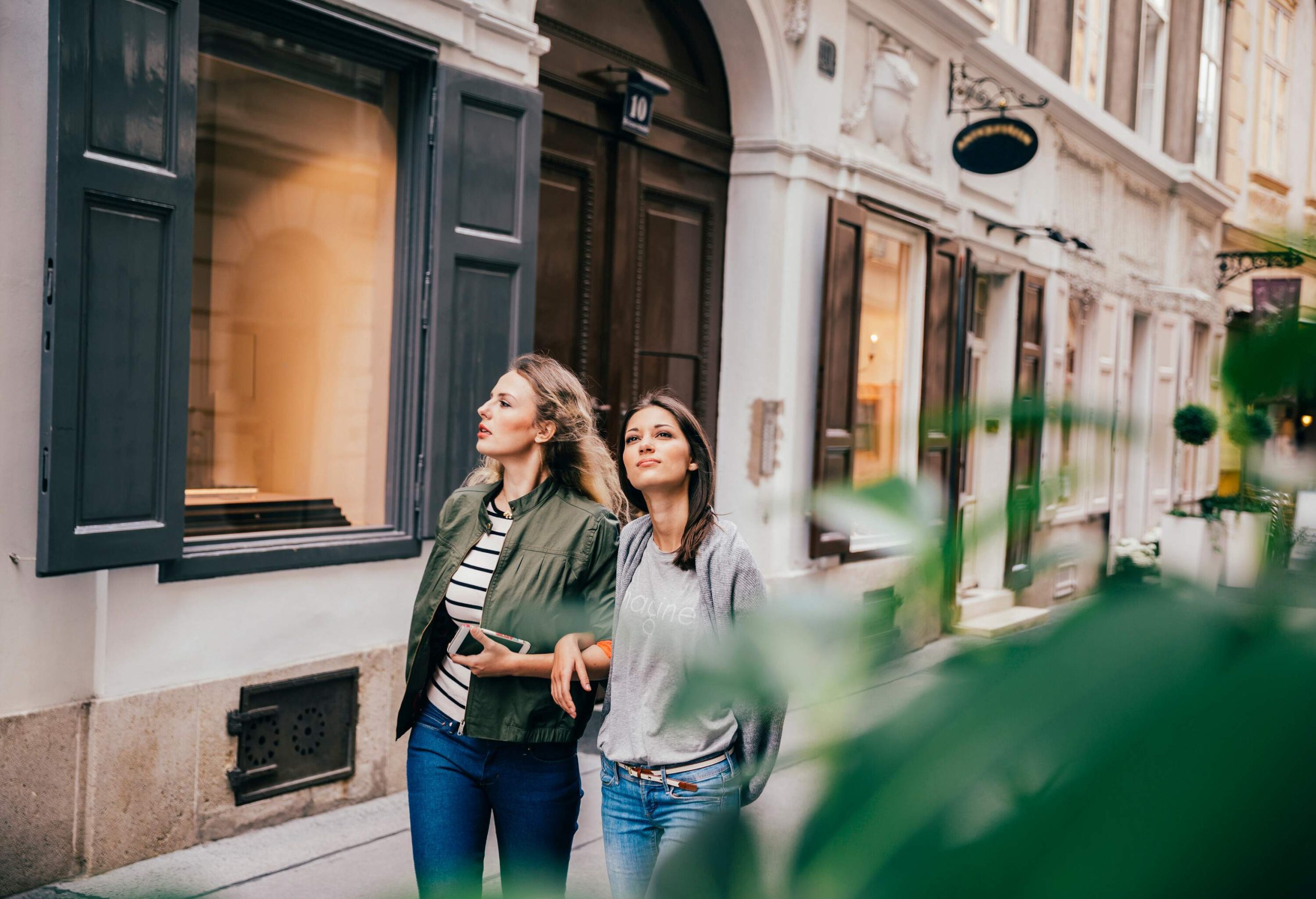 Two women looking around the area as they walk along the sidewalk.