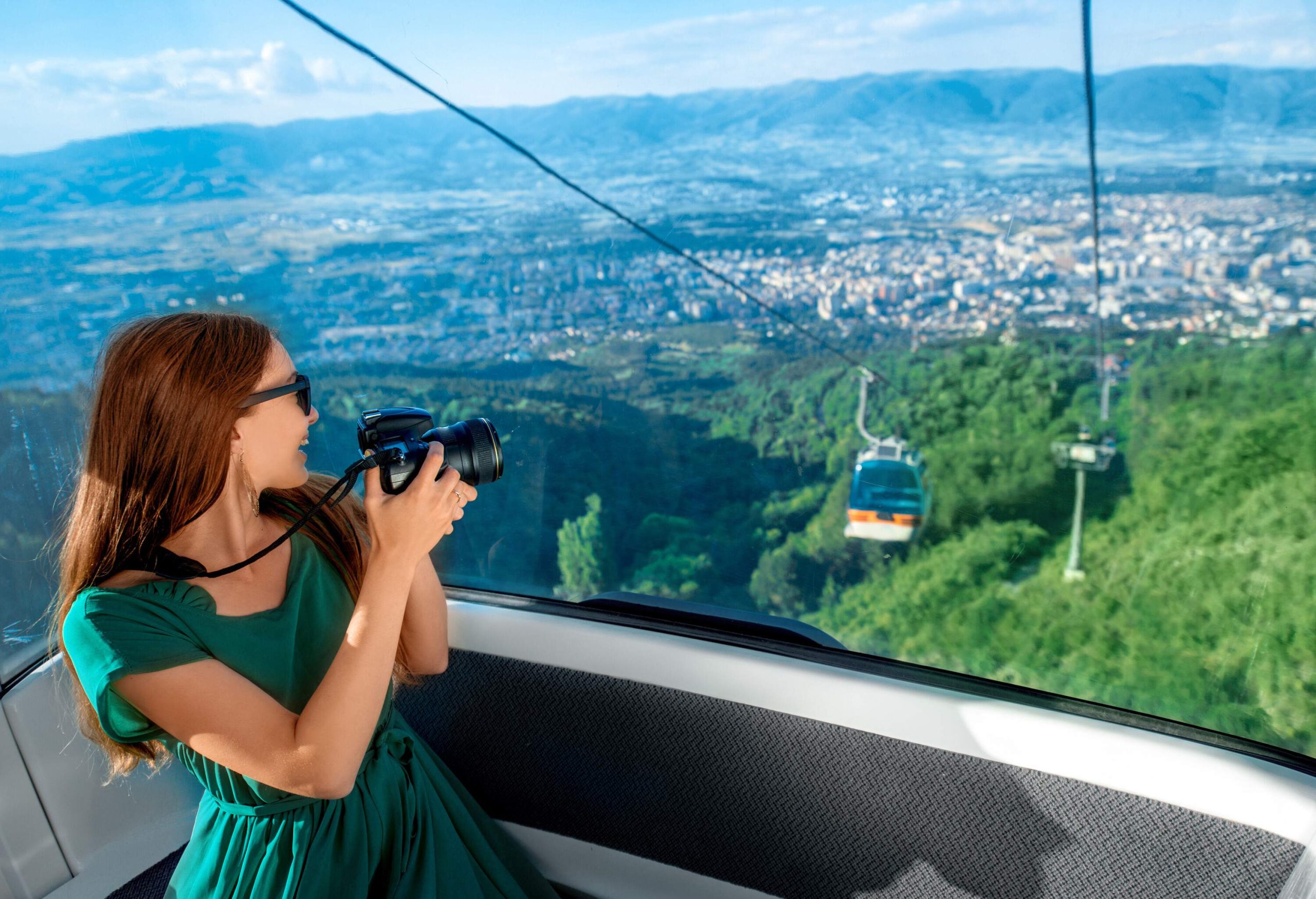 A woman aboard a cable car staring out the window with a camera.