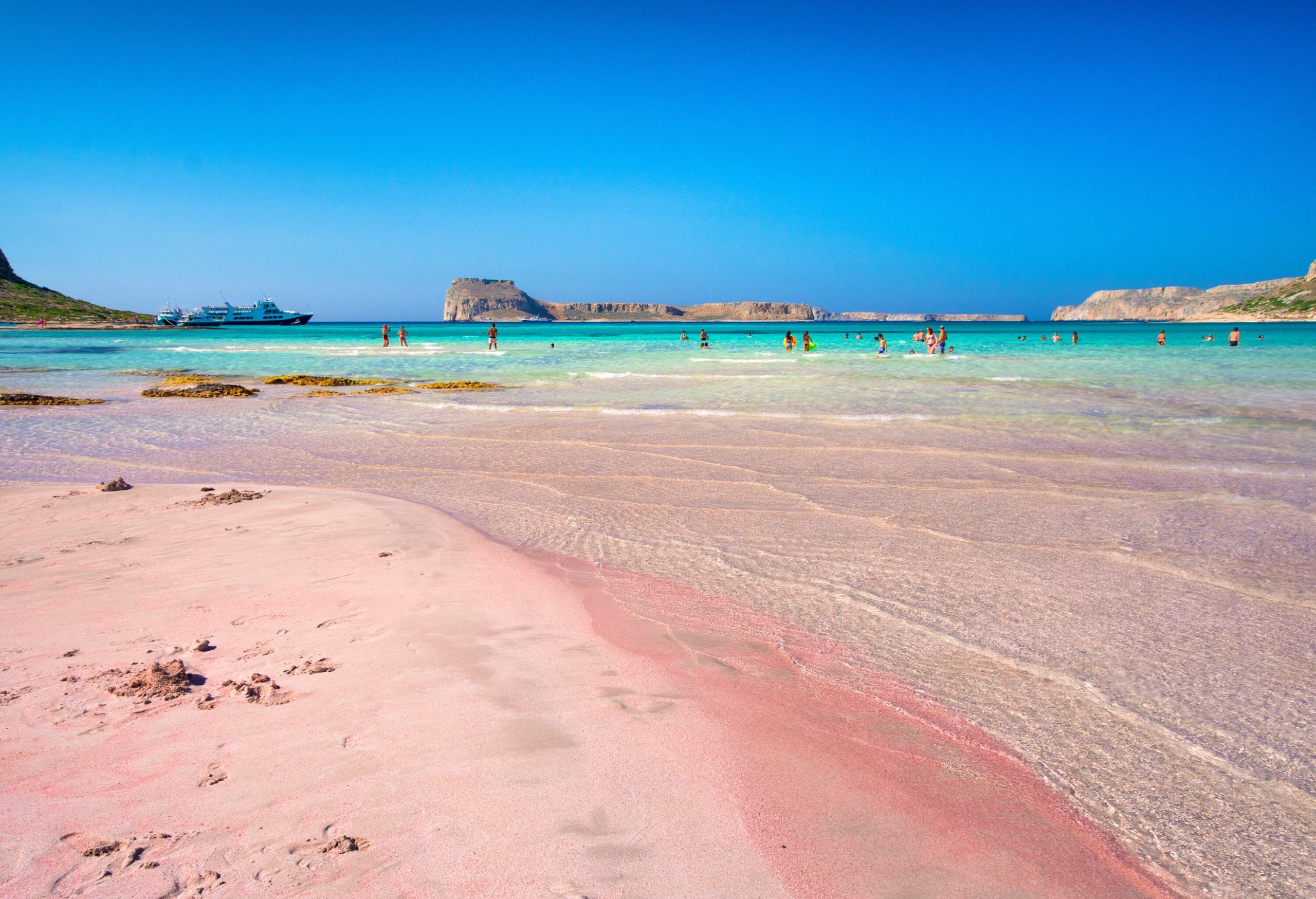 People on the turquoise water beach with a pinkish sand shore.